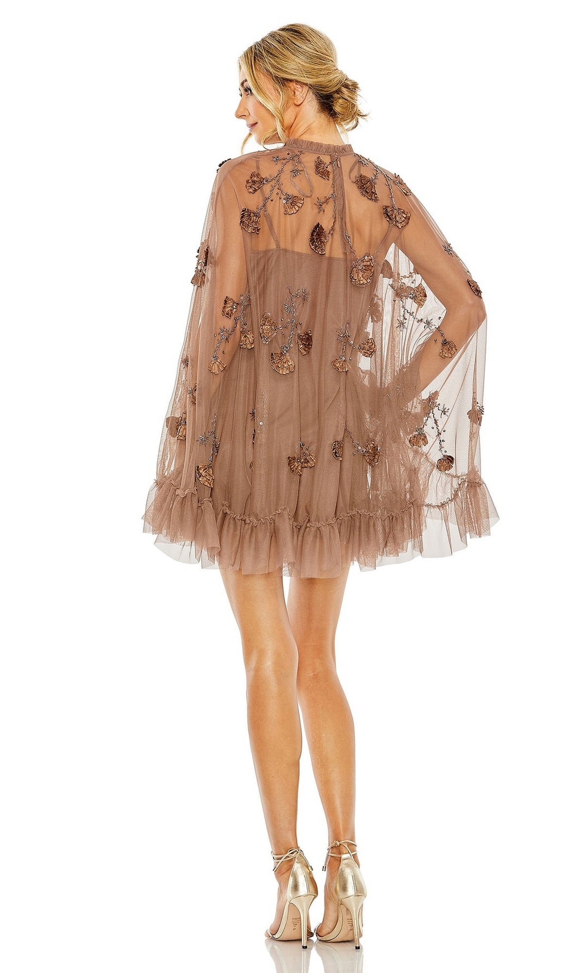 A woman with her hair in an updo stands with her back to the camera, wearing the Long Sleeve Short Hoco Dress: Mac Duggal 9257—a sheer brown party dress featuring floral appliqués and a ruffled hem.
