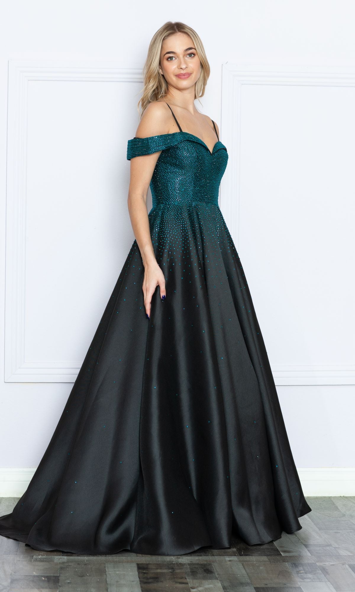 Woman wearing the Cold-Shoulder Beaded Long Prom Ball Gown 9278, a teal and black long A-line dress with thin straps, standing indoors against a white wall on a wooden floor.