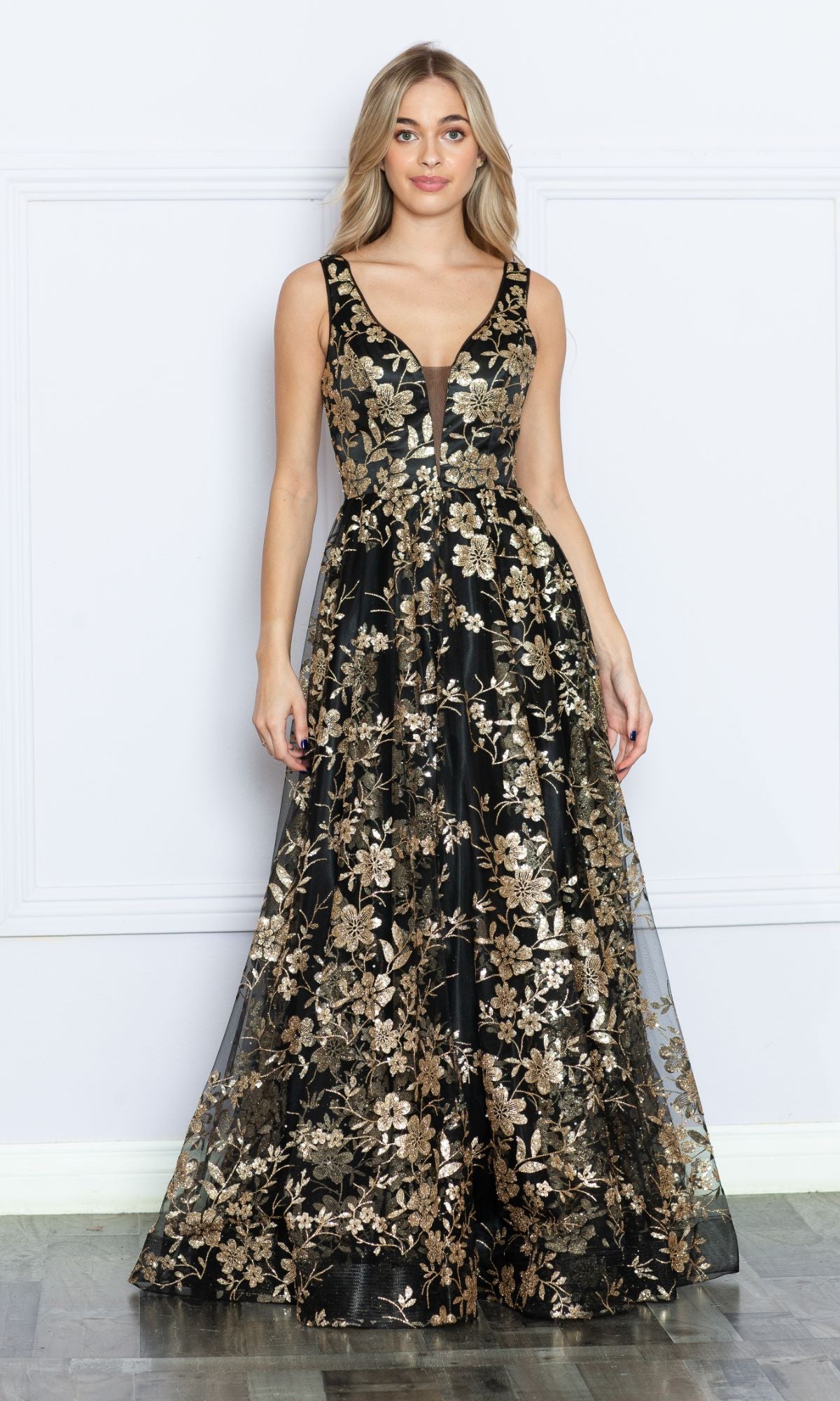 A woman stands against a plain light-colored wall in the Glitter-Floral-Print Long A-Line Prom Dress 9298, a sleeveless black v-neck gown featuring gold floral embroidery.