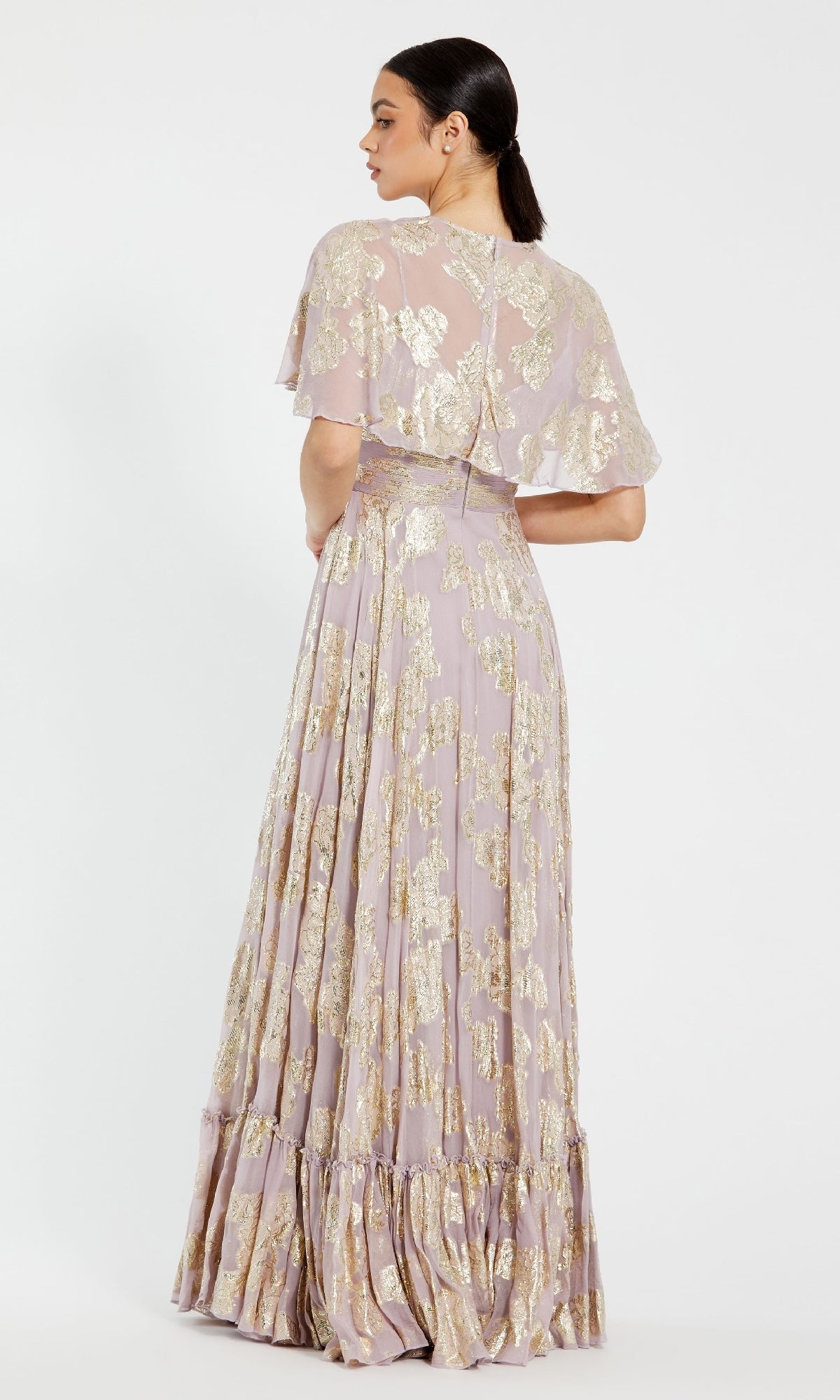 Woman in the Caped Long Lilac Formal Dress by Mac Duggal 9304, featuring gold floral patterns and a layered cape, standing with her back to the camera against a plain background.