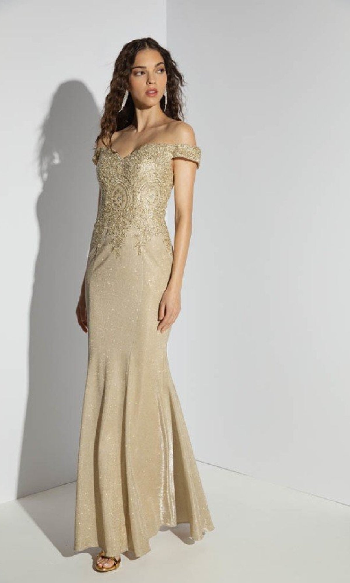 A woman wears the Off-Shoulder Long Glitter Prom Dress: Eureka 9306, a floor-length gold gown with intricate beadwork, standing against a plain light background.
