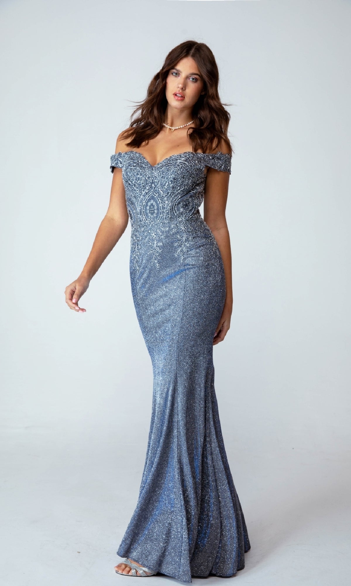 A woman stands against a plain light background wearing the Off-Shoulder Long Glitter Prom Dress Eureka 9306—a fitted, sparkly blue evening gown with a slight mermaid silhouette.
