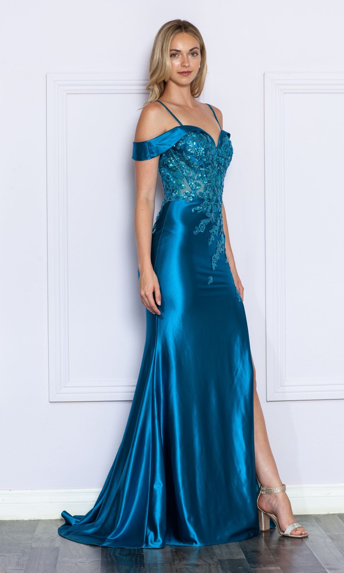 A woman models the Embellished Off-the-Shoulder Long Prom Dress 9350 in teal satin, featuring sequin details and a thigh-high slit, against a light-colored wall.