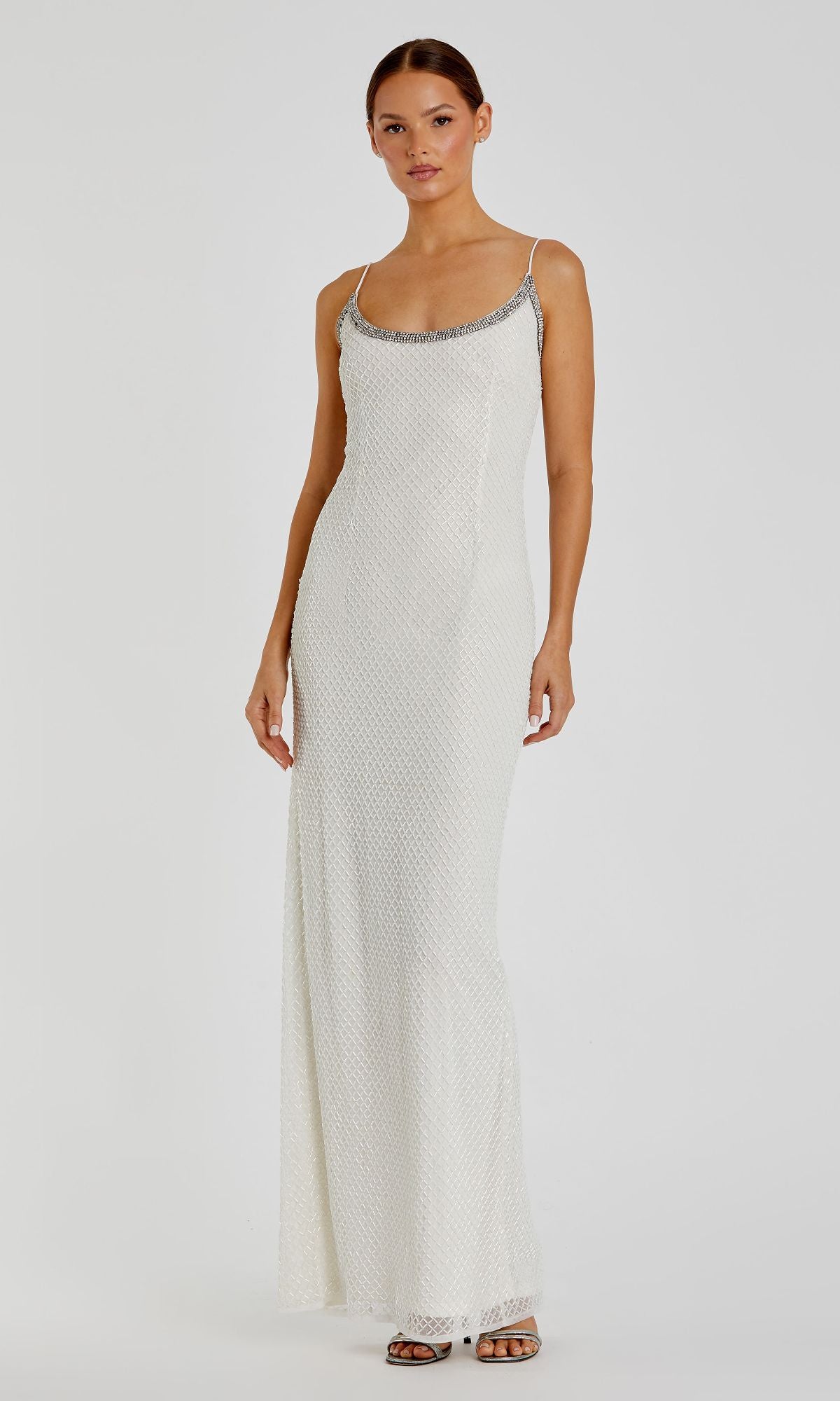 A woman poses against a plain light background wearing the Sleek Long Beaded Prom Dress by Mac Duggal 93551, a sleeveless gown with thin straps and silver embellishments at the neckline.