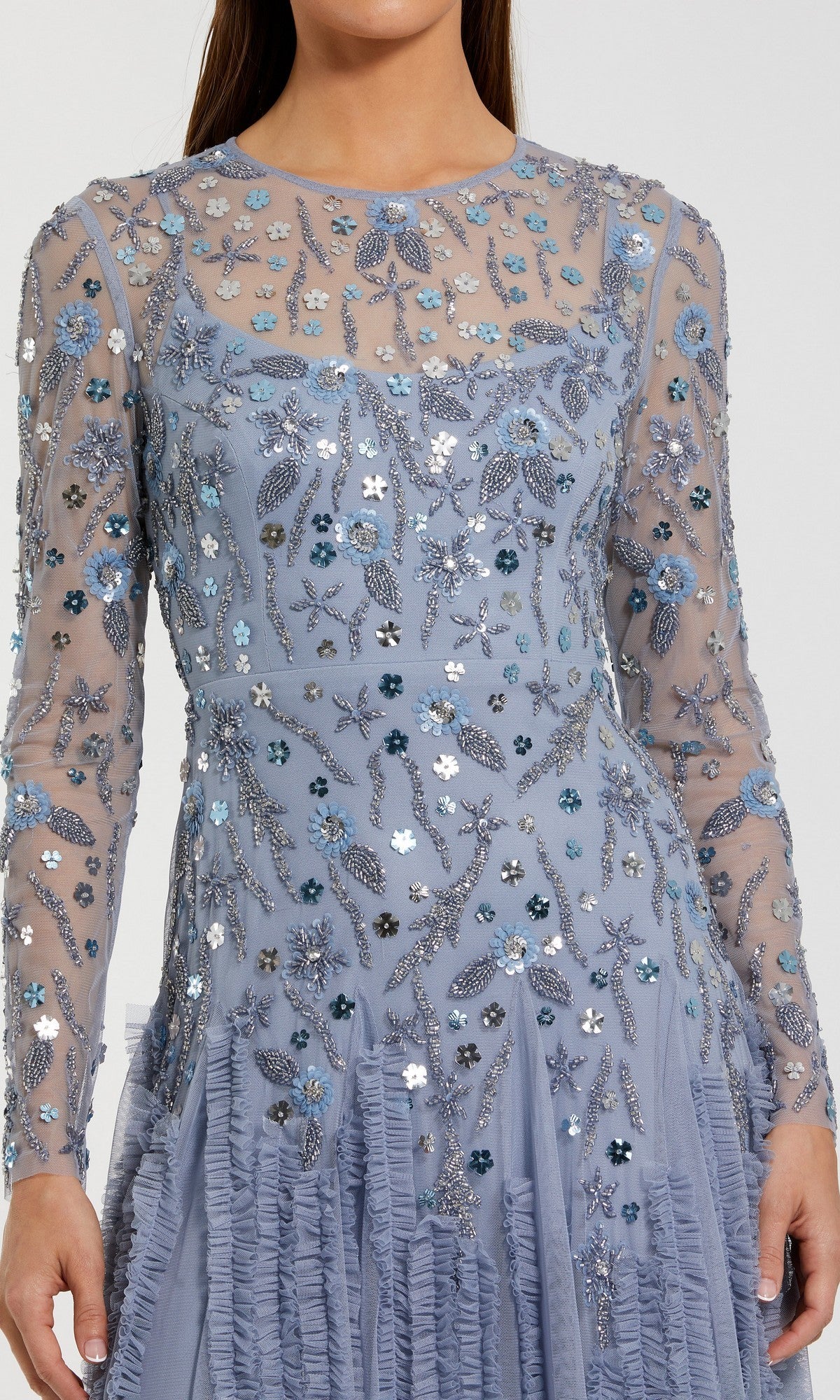 A person wearing the Mac Duggal 9357 long formal dress, featuring light blue sheer fabric embellished with intricate floral embroidery and sparkling sequins.