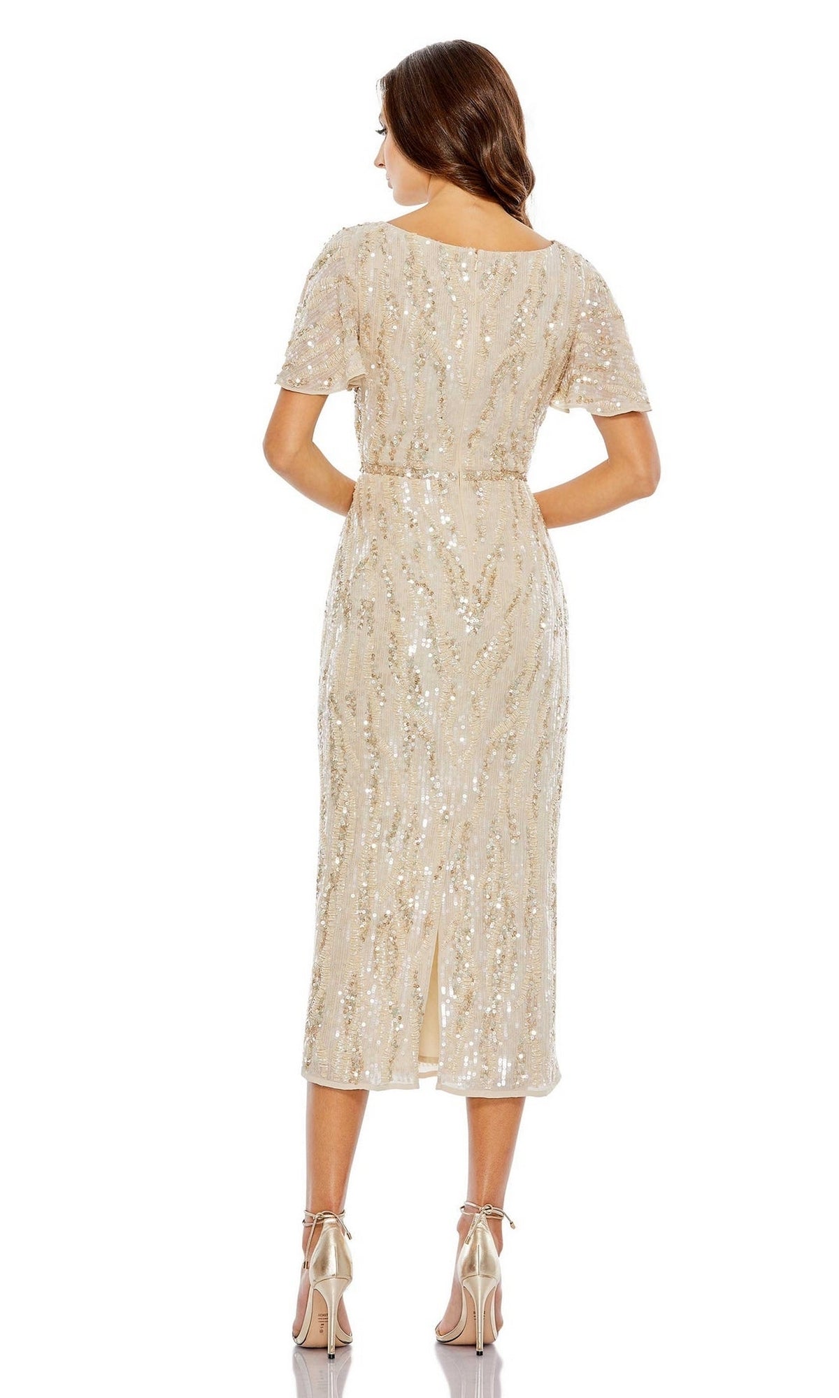 A woman stands facing away in the Short Wedding Guest Dress 93591 by Mac Duggal, a fitted, knee-length beige sequin dress with short sleeves, back slit, and paired with high-heeled sandals.