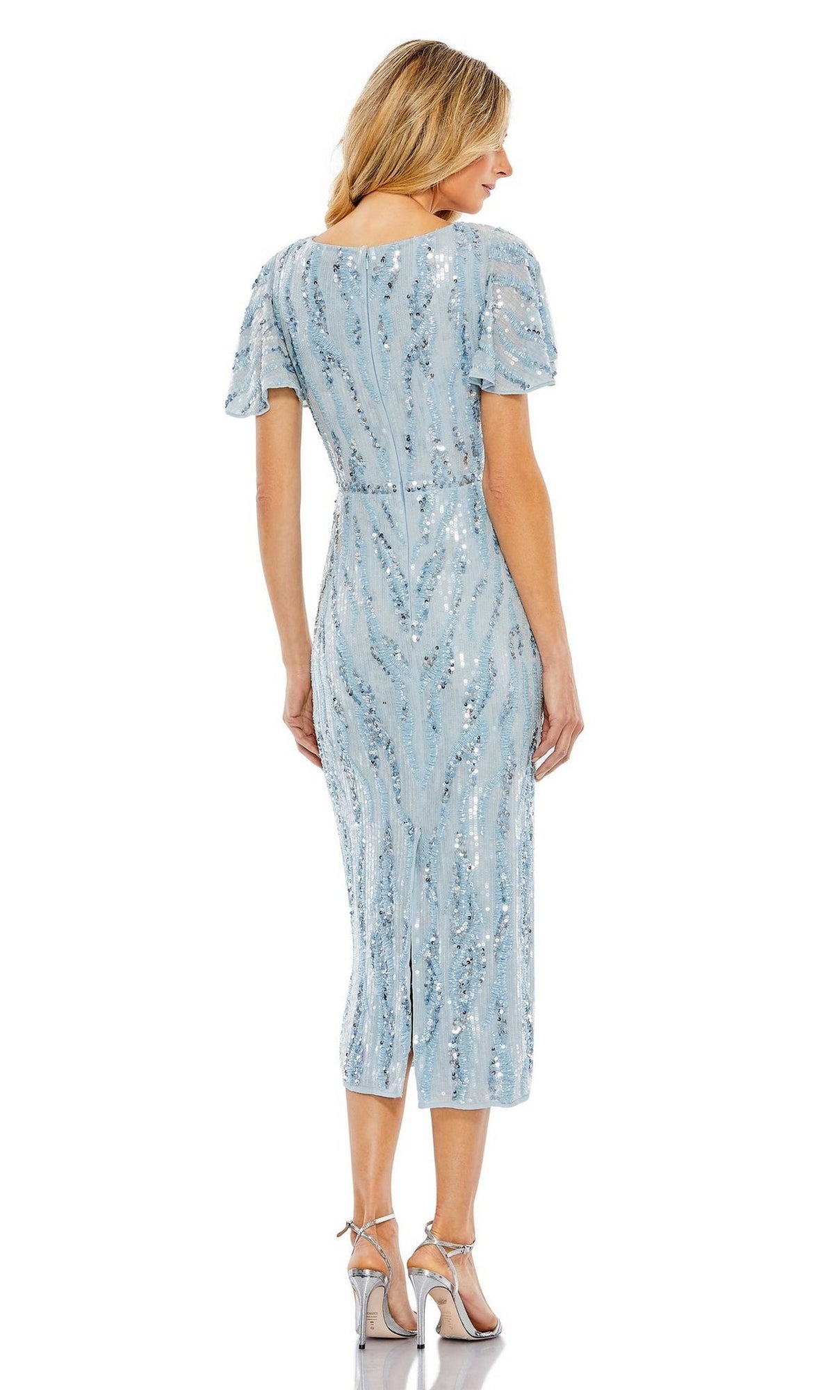 A woman faces away, wearing the Short Wedding Guest Dress 93591 by Mac Duggal—a light blue, beaded midi dress with short sleeves—paired with silver high-heeled sandals.