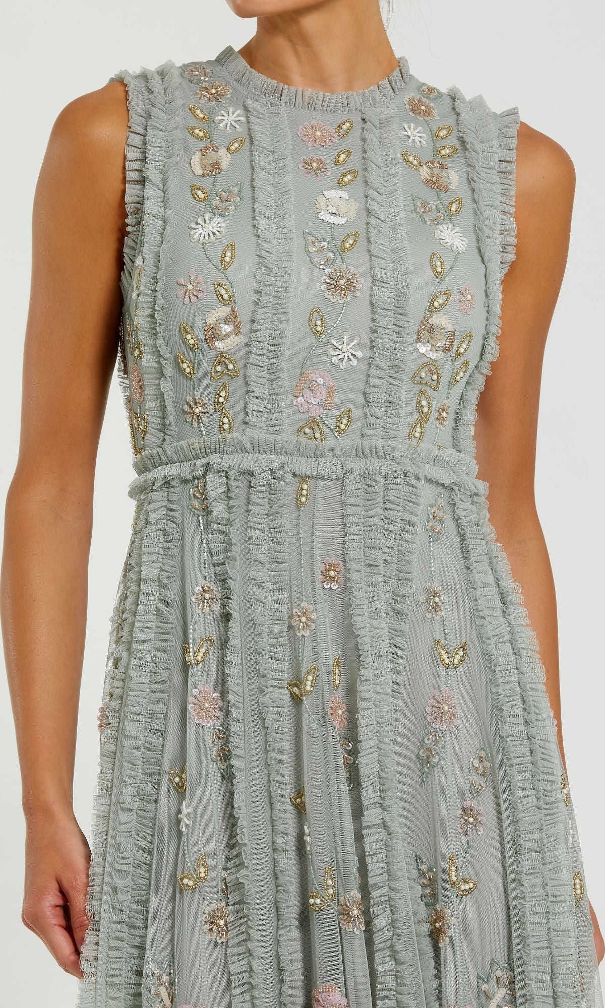 A person with light brown skin wears the Sleeveless Long Sage Formal Dress by Mac Duggal (9360), featuring ruffled trim and pastel floral embroidery, reflecting classic evening elegance.
