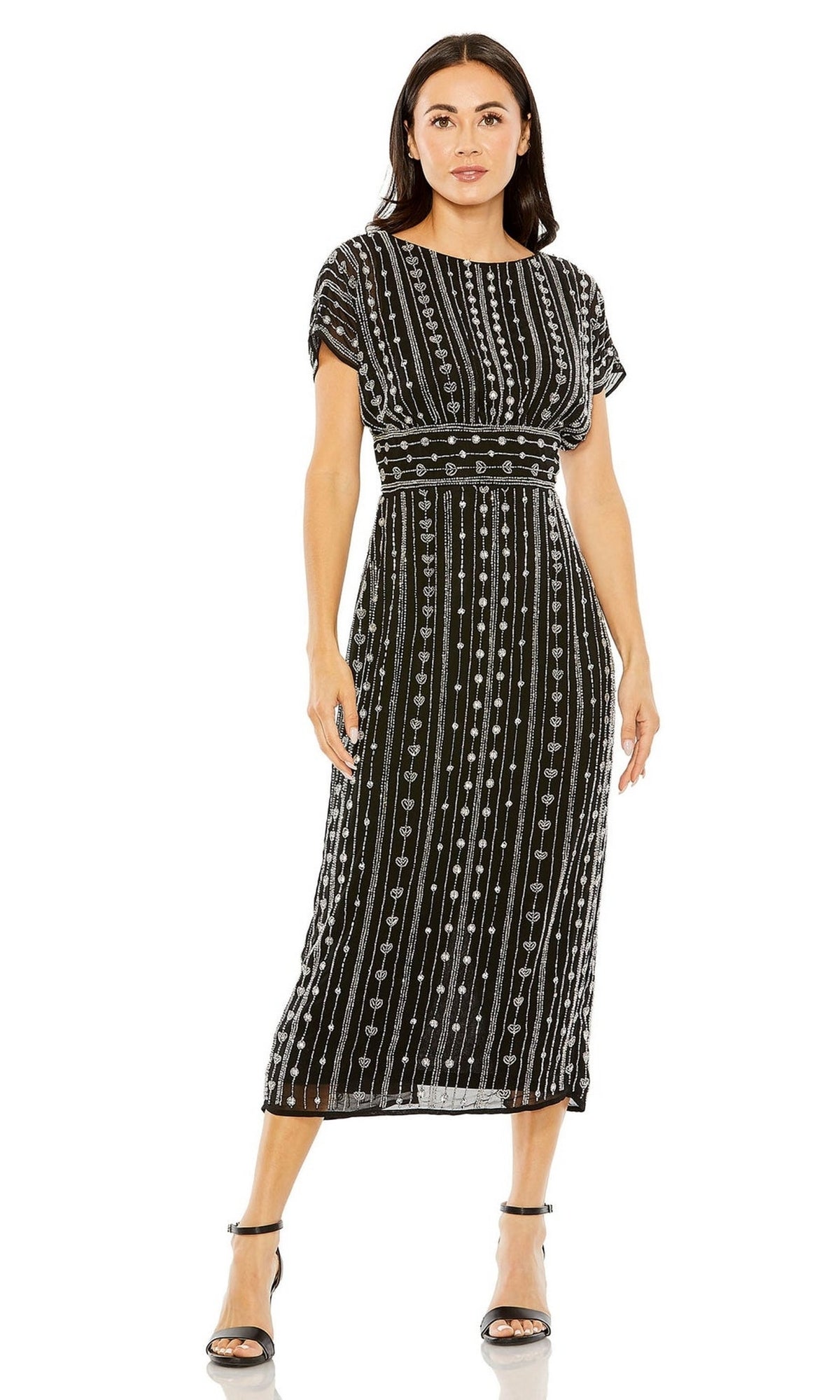 A woman wears the Mac Duggal Beaded Short Wedding-Guest Dress 93649, a black midi dress with vertical white bead patterns and short sleeves, paired with black strappy heels, against a plain white background.