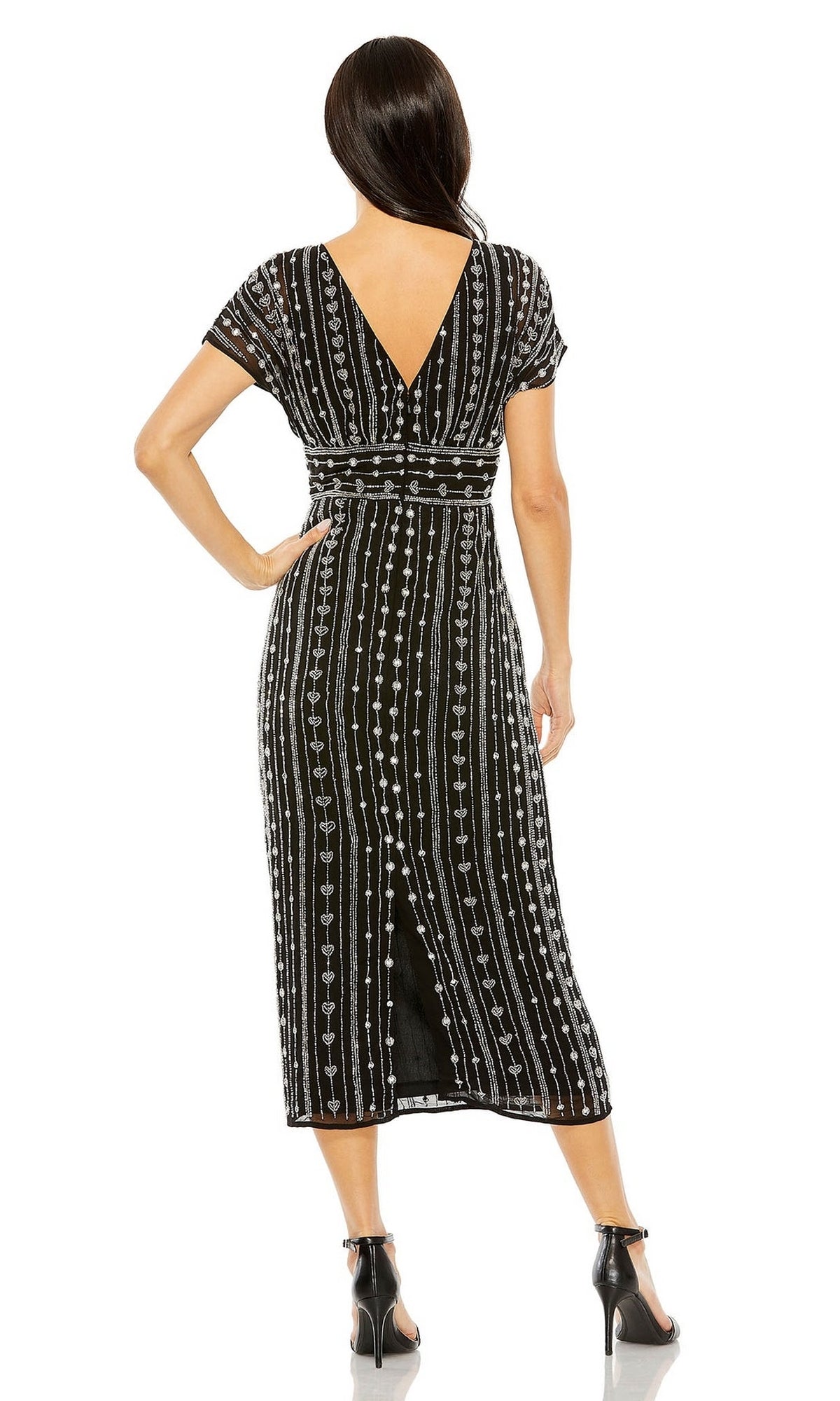 A woman faces away, wearing the Mac Duggal Beaded Short Wedding-Guest Dress 93649 with white vertical patterns and a deep V-back, paired with black high-heeled sandals.