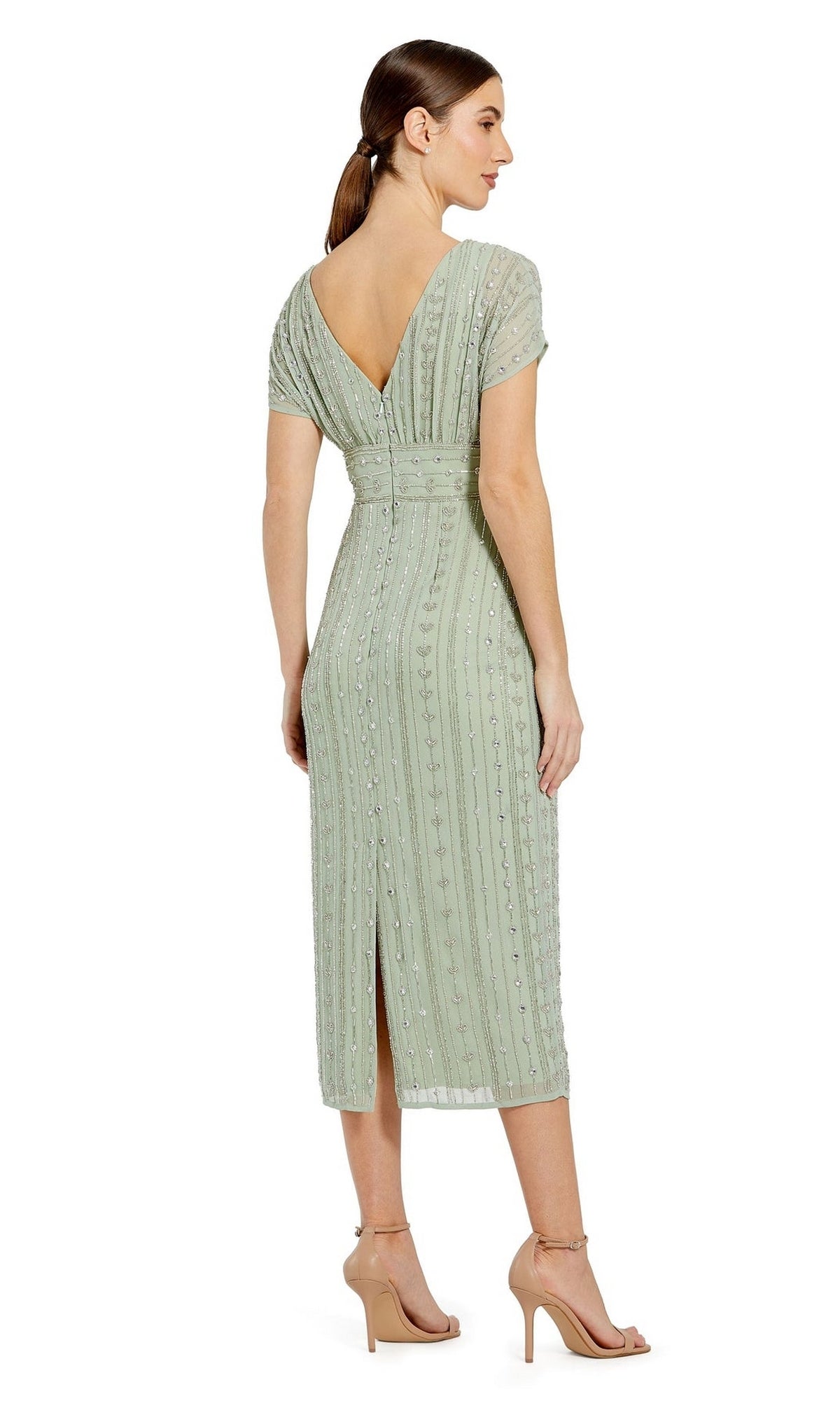 A woman in the Mac Duggal Beaded Short Wedding-Guest Dress 93649, featuring light green beads, short sleeves, knee-length hem, V-back neckline, and beige heeled sandals stands against a white background.