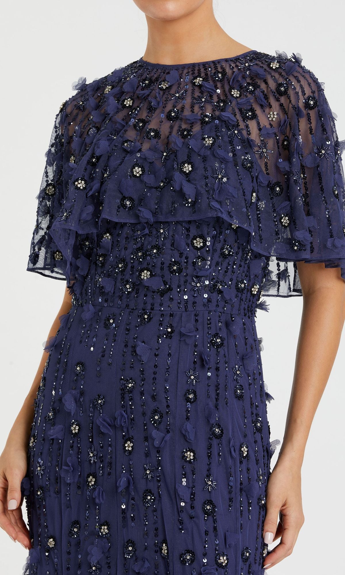 A woman wears the Mac Duggal 93653 Beaded-Cape Long Formal Dress in navy, featuring layered sheer fabric, floral embroidery, and elegant beaded embellishments.
