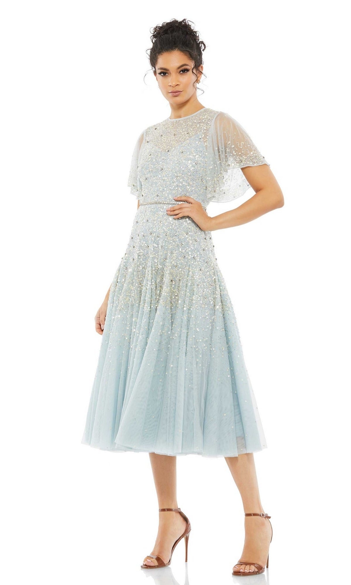 Woman wearing the Mac Duggal 93655 short wedding guest dress in light blue with sequins, sheer overlay, and short sleeves, paired with strappy high-heeled sandals.