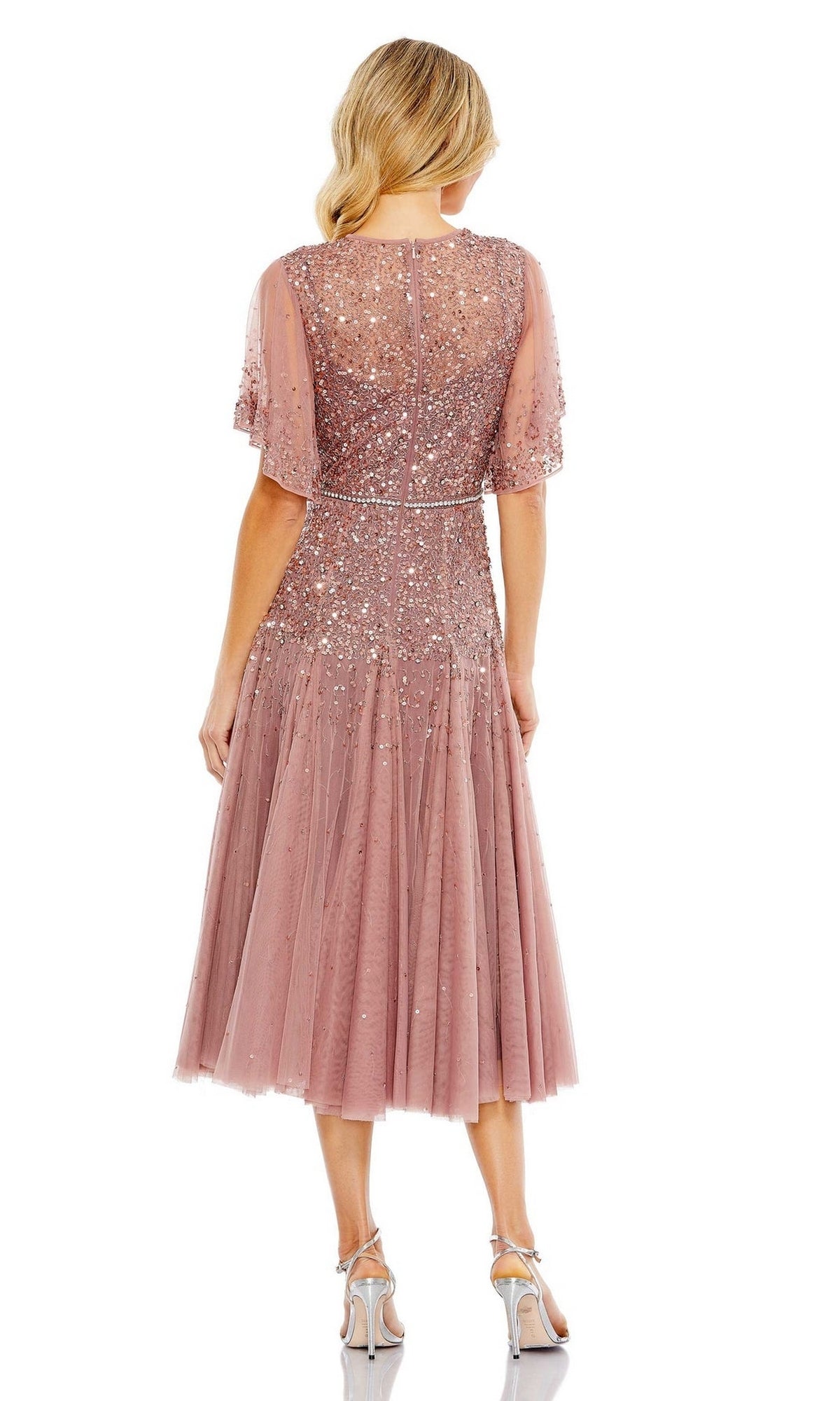 A woman faces away, wearing the Mac Duggal 93655 short mauve wedding guest dress with sequin embellishments, sheer sleeves, and paired with strappy heels.