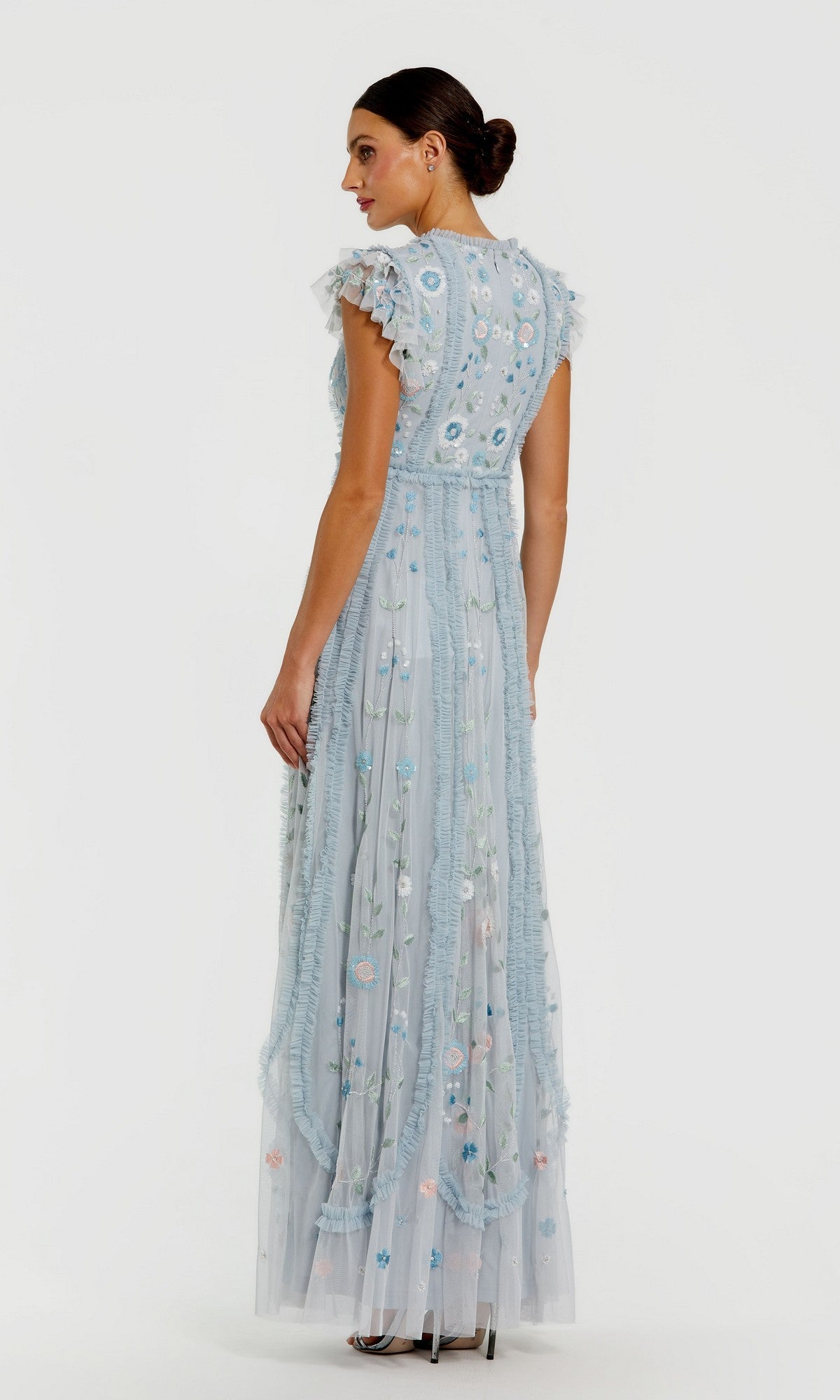 A woman in the Mac Duggal 9366 long formal dress—a light blue, floor-length gown with floral embroidery and flutter sleeves—stands sideways against a plain white background.
