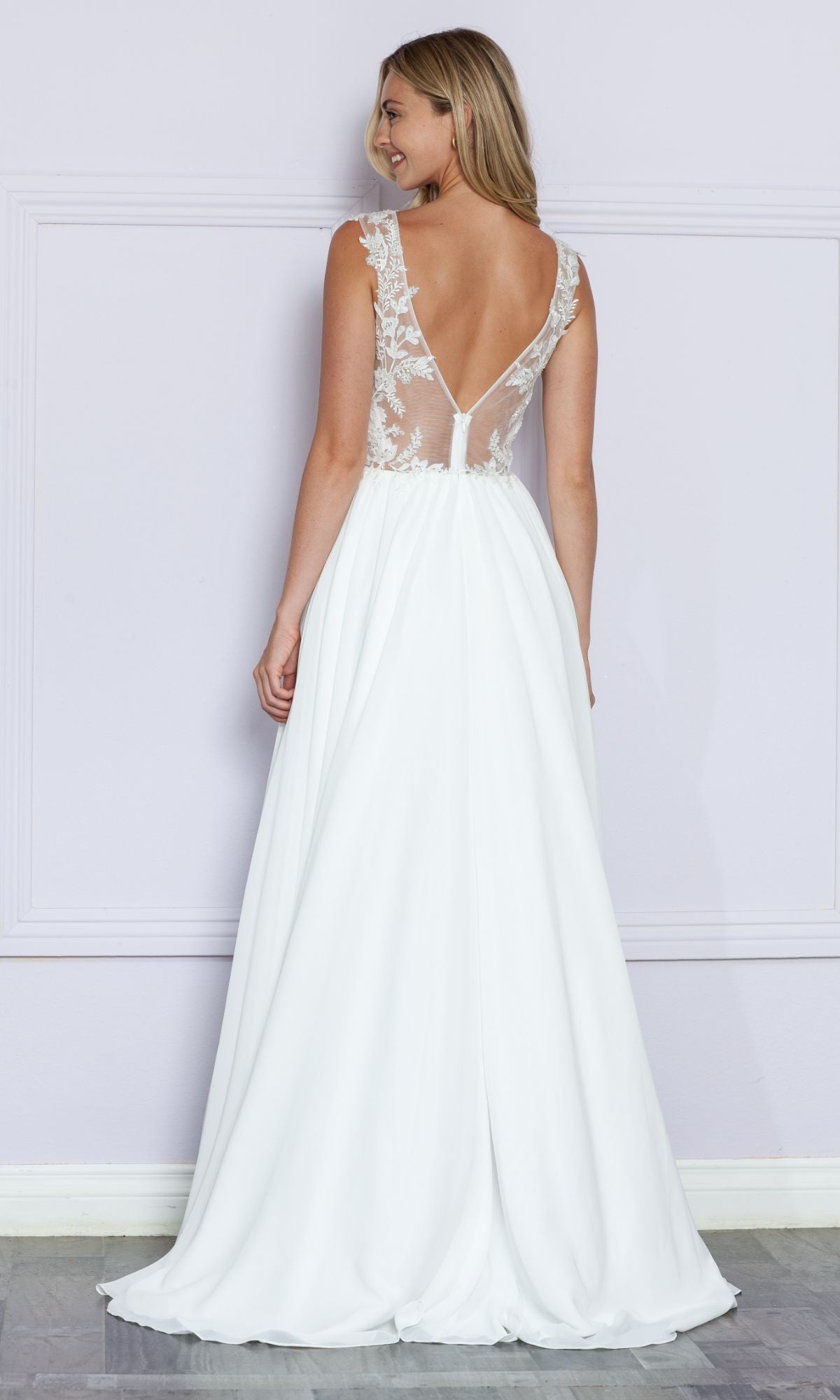 A woman faces away from the camera, wearing the Sheer-Lace Bodice Long White Formal Dress 9376, featuring a sheer-lace bodice and flowing skirt, standing against a pale wall.