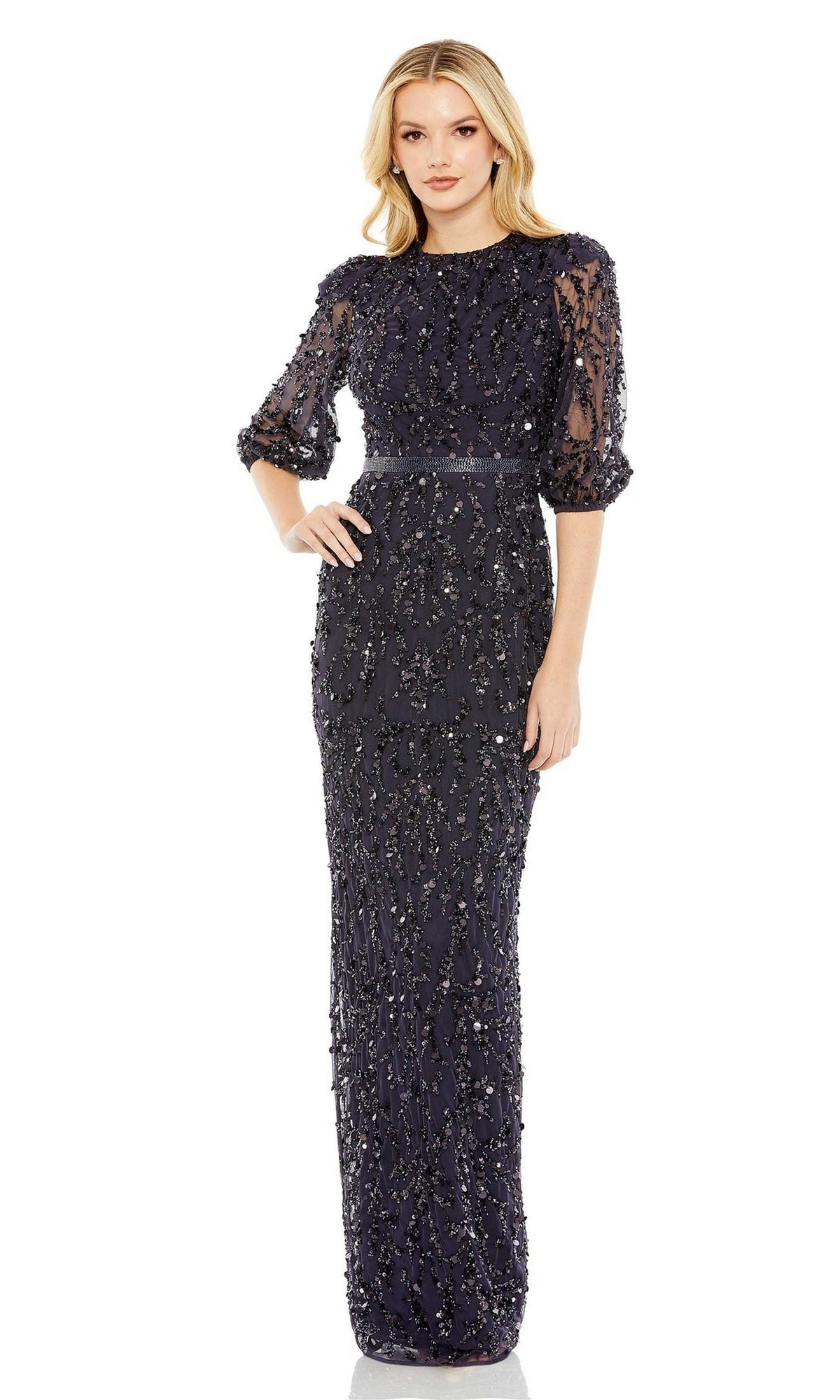 A woman stands against a white background wearing the Mac Duggal 93790 Long Sleeve Beaded Formal Dress, featuring a high neck, sheer sleeves, and intricate embellishments.