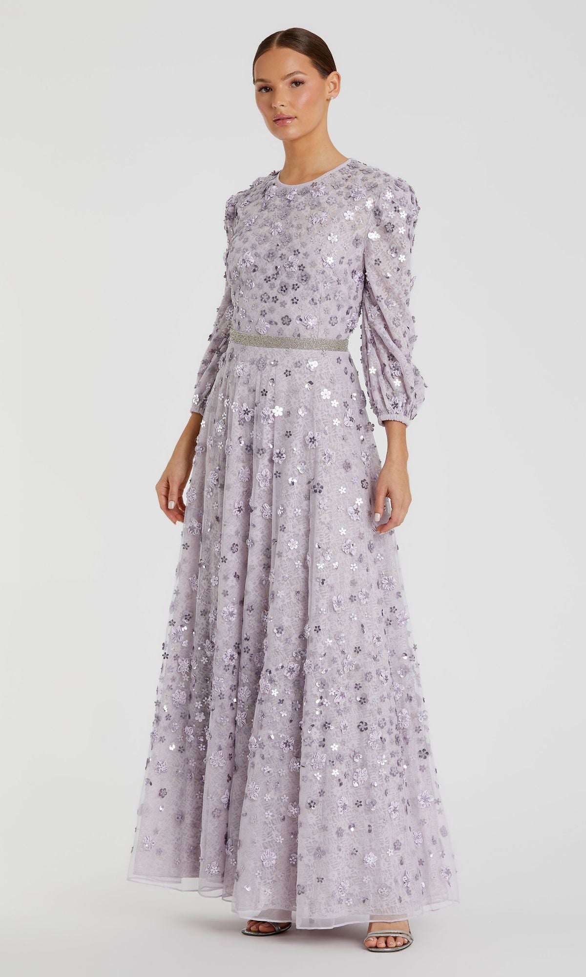 A woman wears the Modest Long Sleeve Formal Dress: Mac Duggal 93805 in lilac, featuring floral embellishments and three-quarter sleeves, standing against a plain background.