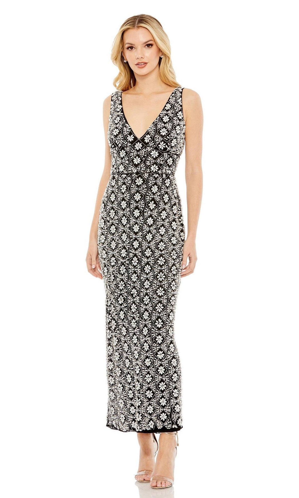 A woman wears the Mac Duggal Short Wedding Guest Dress 93807, a semi-formal sleeveless V-neck dress with a white floral pattern and fitted ankle-length silhouette, paired with neutral heels against a plain background.