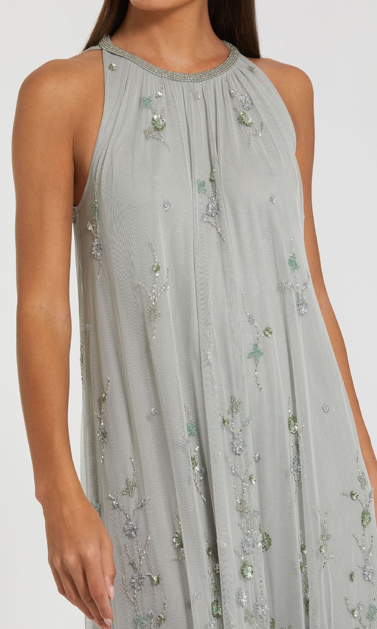 A woman wearing the Sage Green Long Formal Dress by Mac Duggal 9382, a sleeveless trapeze style with silver and sage green floral beading and light grey accents.