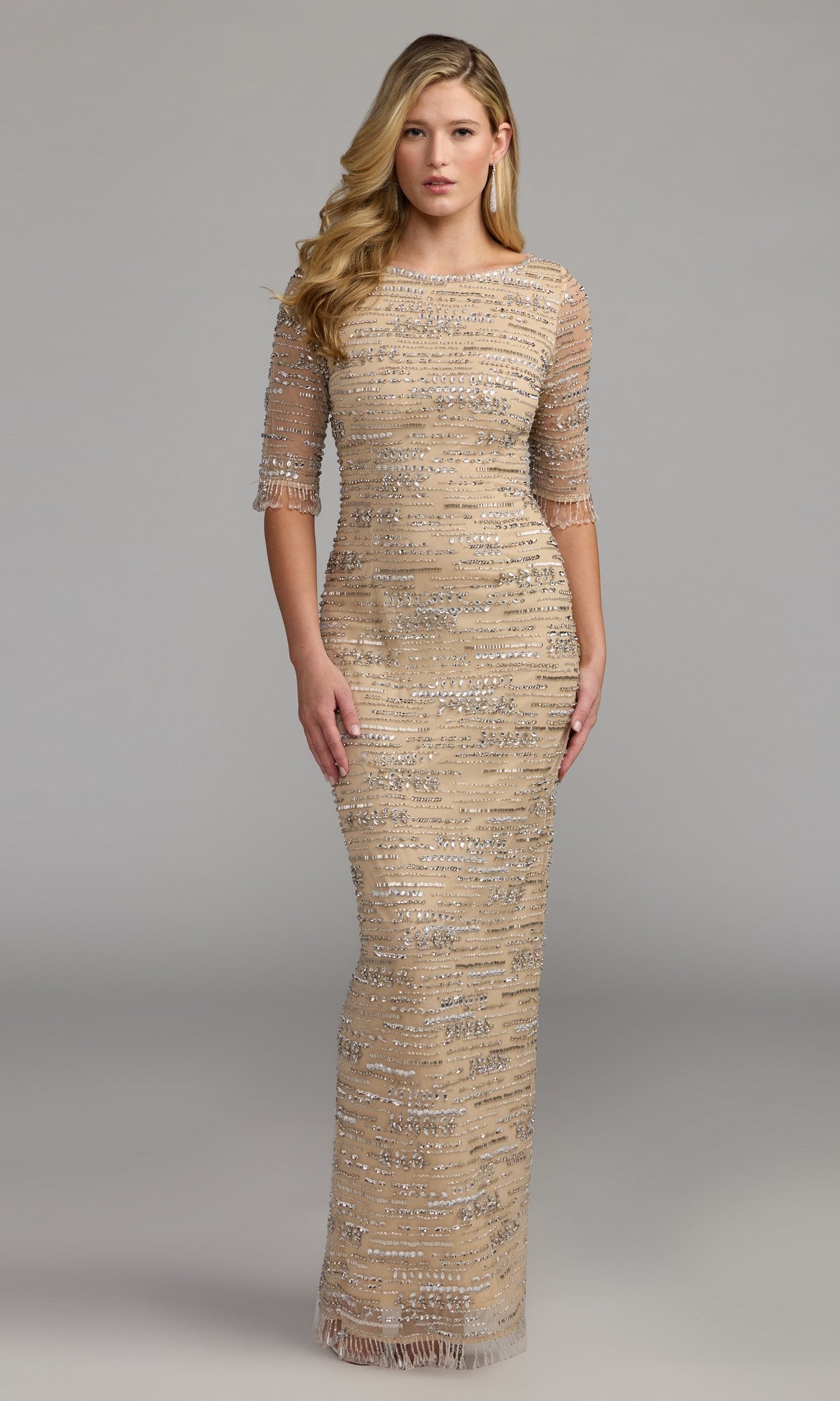 A woman wearing the Mac Duggal 93832 long formal dress in nude, featuring a fitted silhouette with silver sequin embellishments and sheer three-quarter sleeves, stands against a plain gray background.