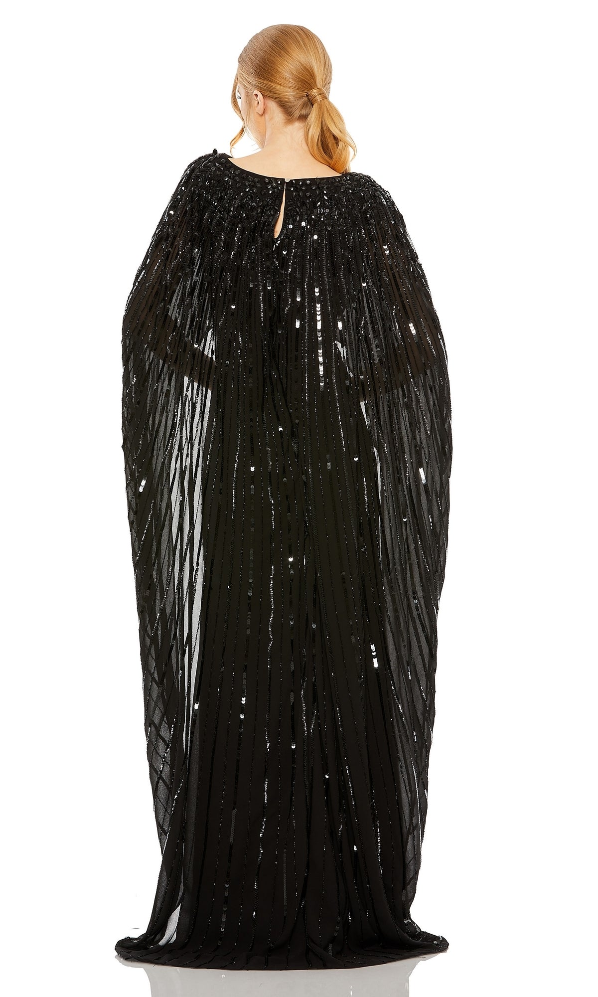 A person faces away, wearing the Mac Duggal 93869 Caped Long Sequin Formal Dress featuring a cape-style silhouette and sheer, draped fabric, with their hair in a low ponytail.