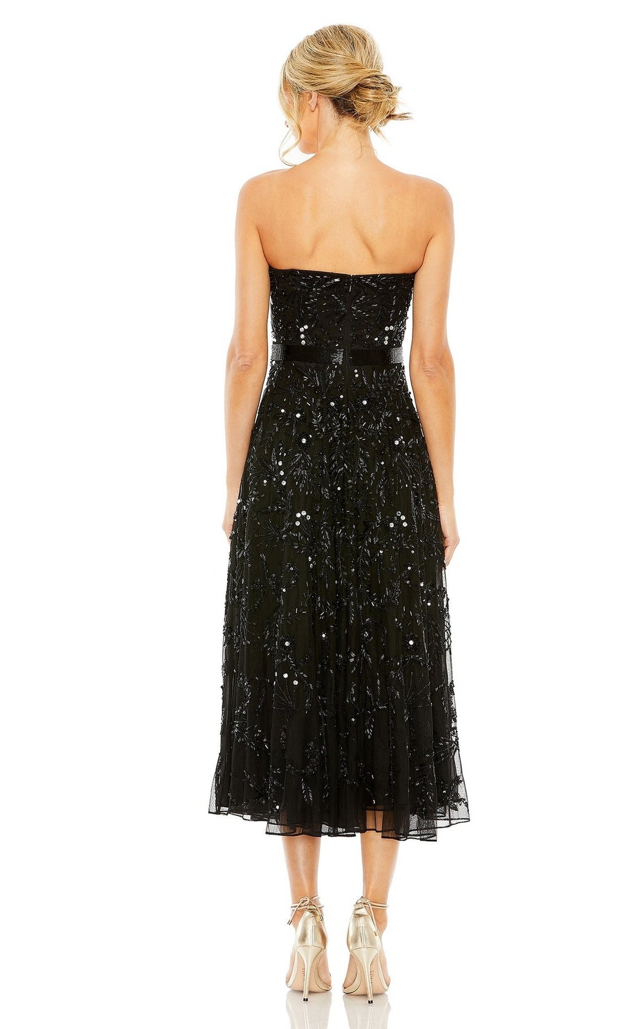 A blonde woman with her hair in an updo is shown from the back wearing the Mac Duggal 93898 strapless wedding guest dress, a black sequined midi party style, paired with gold high heels.