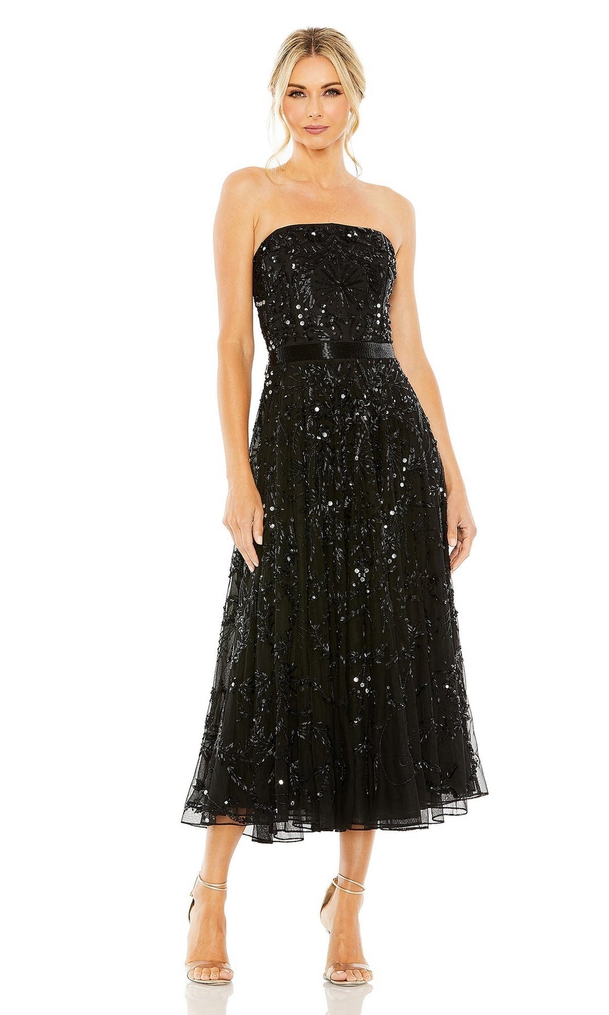 A woman wears the Mac Duggal 93898 Strapless Wedding Guest Dress, a beaded midi dress with black sequin embellishments and a fitted waist, paired with nude heels. The elegant look stands out against a white background.