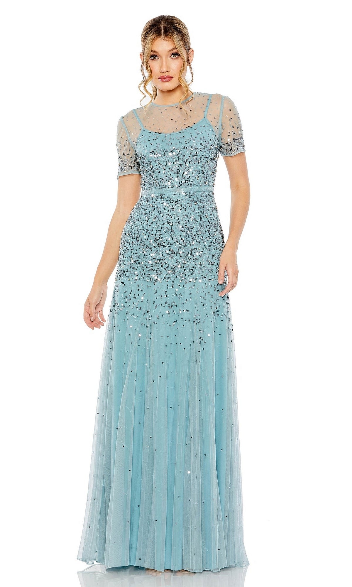 A woman wearing the Mac Duggal Sheer High-Neck Sequin Formal Dress 93909, a floor-length light blue gown with short sheer sleeves and silver embellishments, stands against a white background.