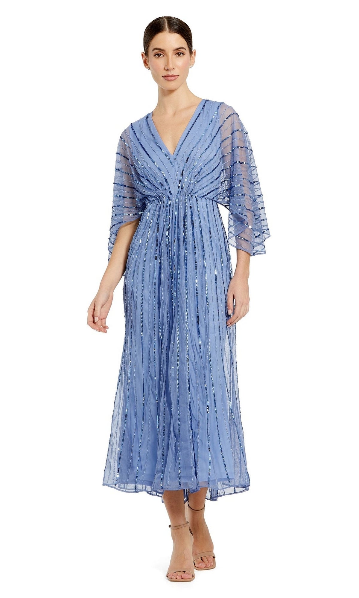 A woman models the Mac Duggal Periwinkle Blue Sequin Formal Dress 93995, featuring kimono sleeves, a V-neckline, and an ankle-length sheer sequin-embellished overlay, standing against a plain white background.