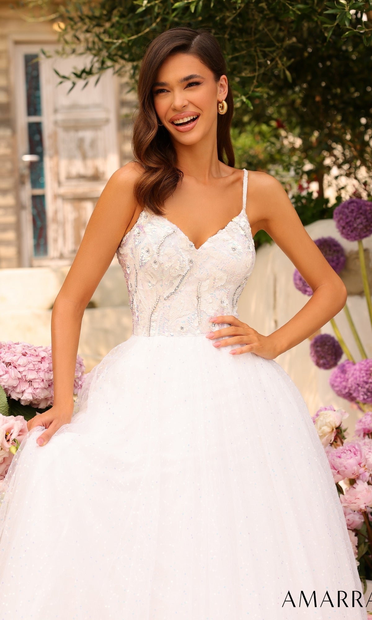 A woman in a white Amarra Sequin-Bodice Long A-Line Prom Dress 94020 stands smiling outdoors, with pink flowers and greenery behind her. The