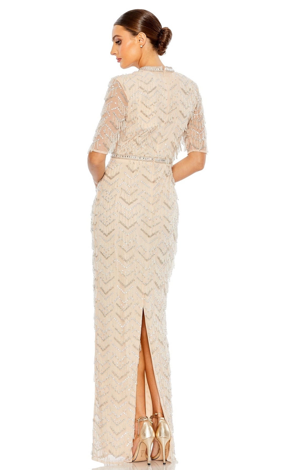 Woman wearing the Mac Duggal Beaded Fringe Long Formal Dress 94071—full-length, nude, with beaded details and short sleeves, features a back slit. She pairs it with metallic heels and is facing away from the camera.