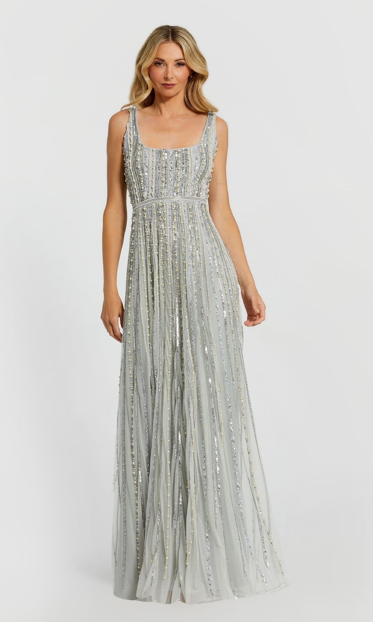 A woman wears the Long Beaded Blue Formal Dress, Mac Duggal 94080—a floor-length, sleeveless gown with vertical sequin embellishments—standing against a plain light background.