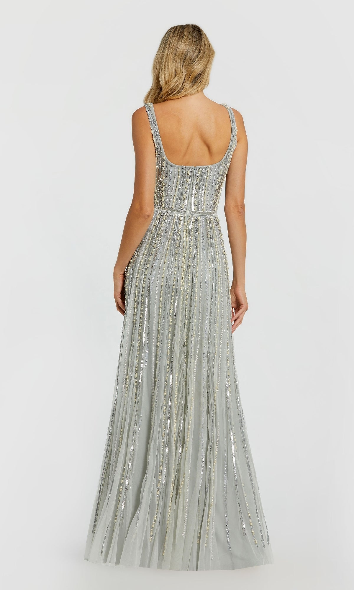 A woman with long blonde hair models the Mac Duggal 94080—a floor-length, sleeveless, blue beaded formal dress—shown from the back against a plain white background.