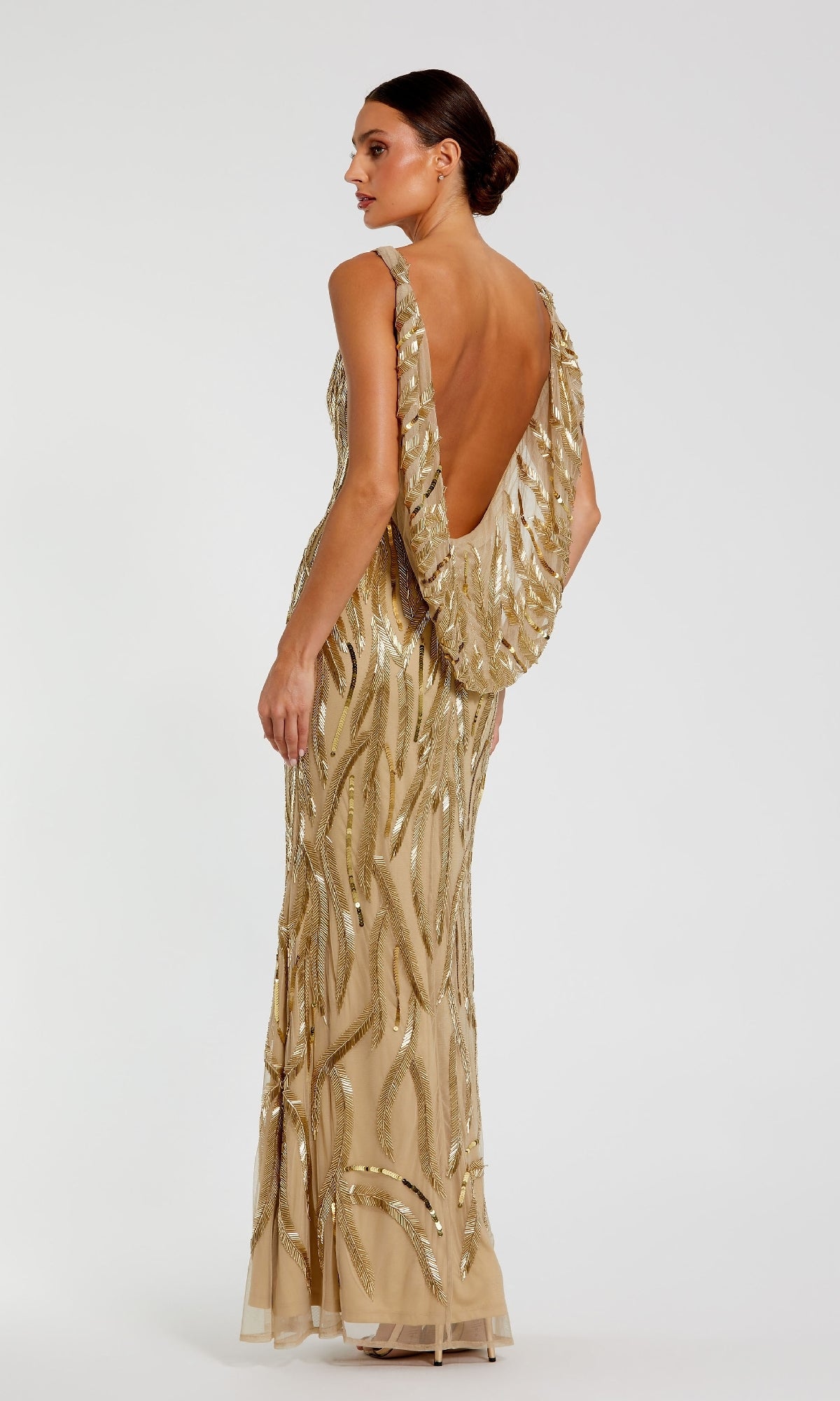 A woman models the Mac Duggal 94146, a floor-length gold formal dress with beaded embellishments and a low draped back, standing against a plain white background.
