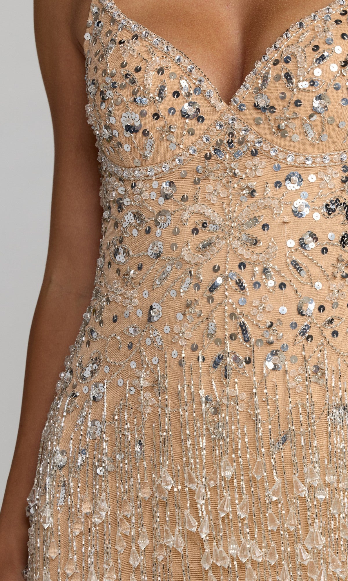 Close-up of the torso and part of one arm of the Long Formal Dress: Mac Duggal 94207, featuring beaded and sequined nude fabric with silver and crystal embellishments, as well as fringe details.