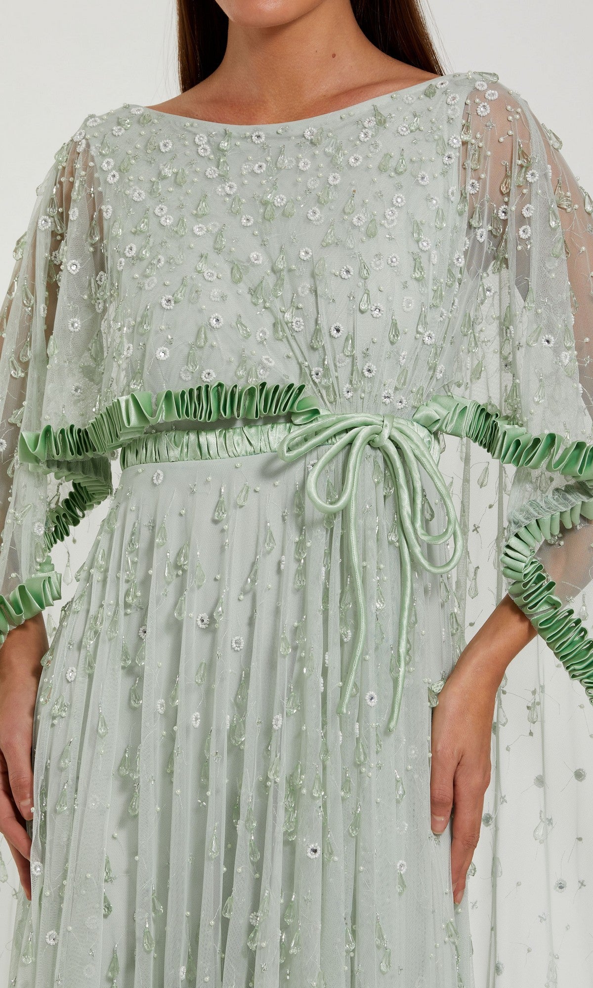Dressed in the Long Formal Dress: Mac Duggal 94294, she wears a sheer, light green gown adorned with sequin and bead embellishments, ruffled trim, and a coordinating ribbon belt at the waist—a stunning interpretation of formal elegance.