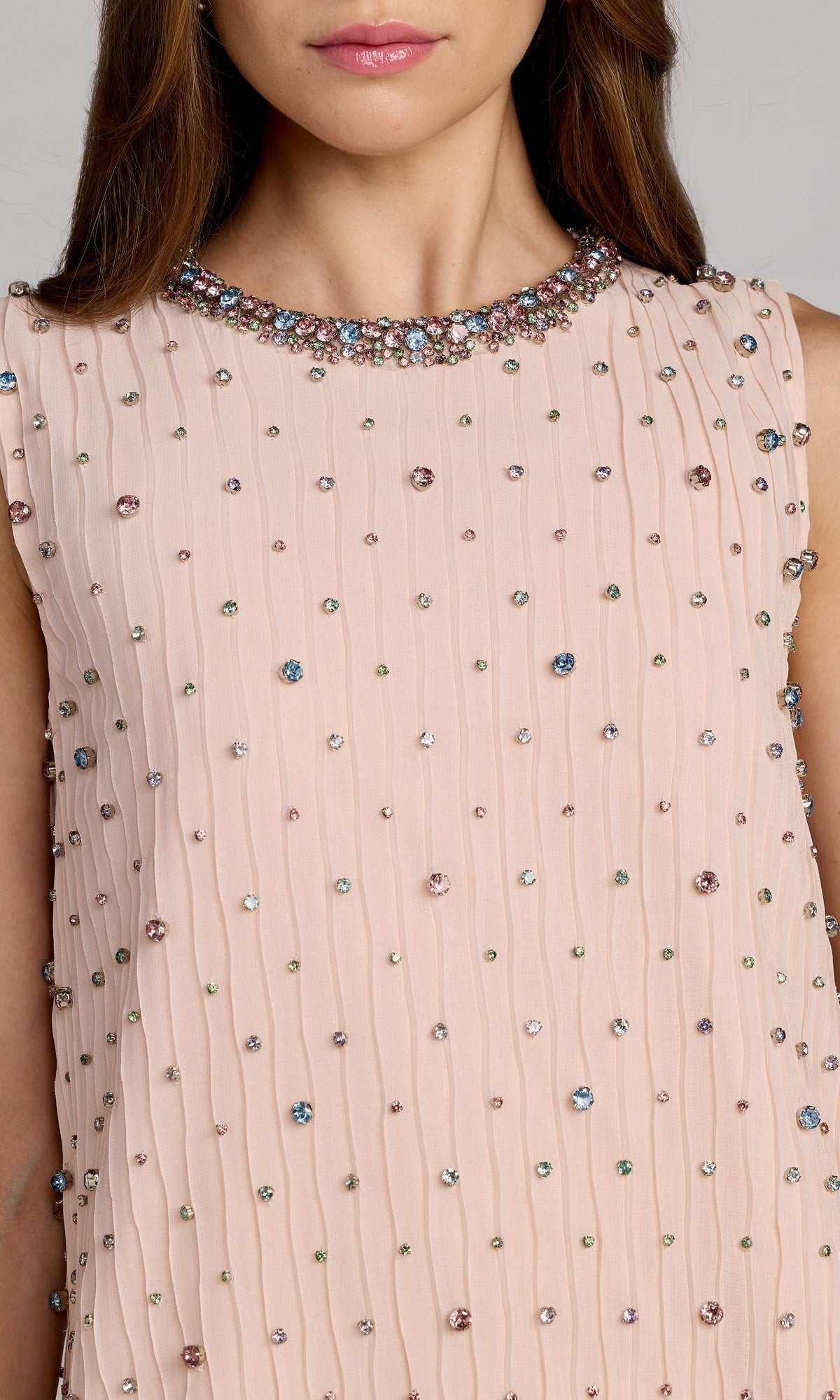 A woman wearing the Mac Duggal 94354 knee-length shift party dress, featuring a sleeveless design in light pink with vertical pleats and multicolored gem embellishments.