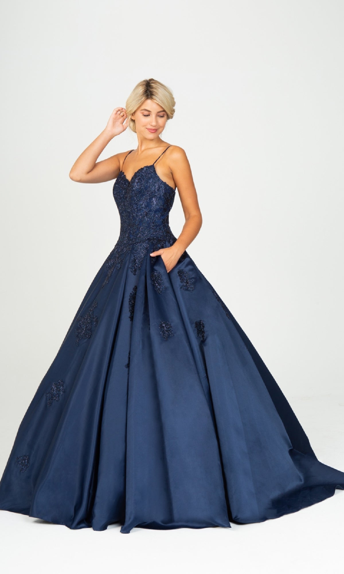 A woman wears the Classic Long Prom Ball Gown: Eureka 9500—navy blue with thin straps, floral embroidery, and a lace-up back—standing against a plain white background.
