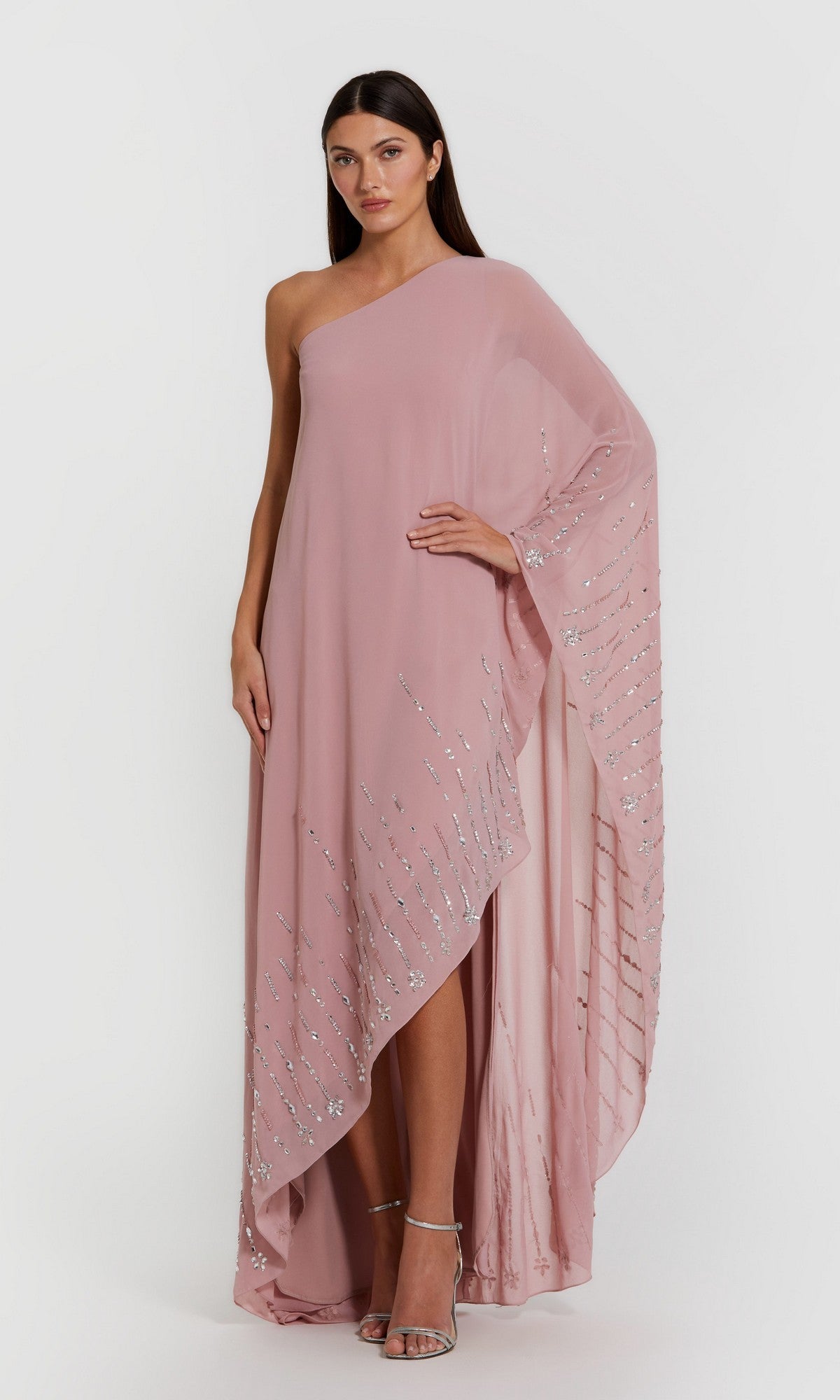 A woman stands against a plain white background wearing the Mac Duggal 9517 long formal dress in antique rose—an elegant one-shoulder kaftan gown embellished with silver sequin detailing.