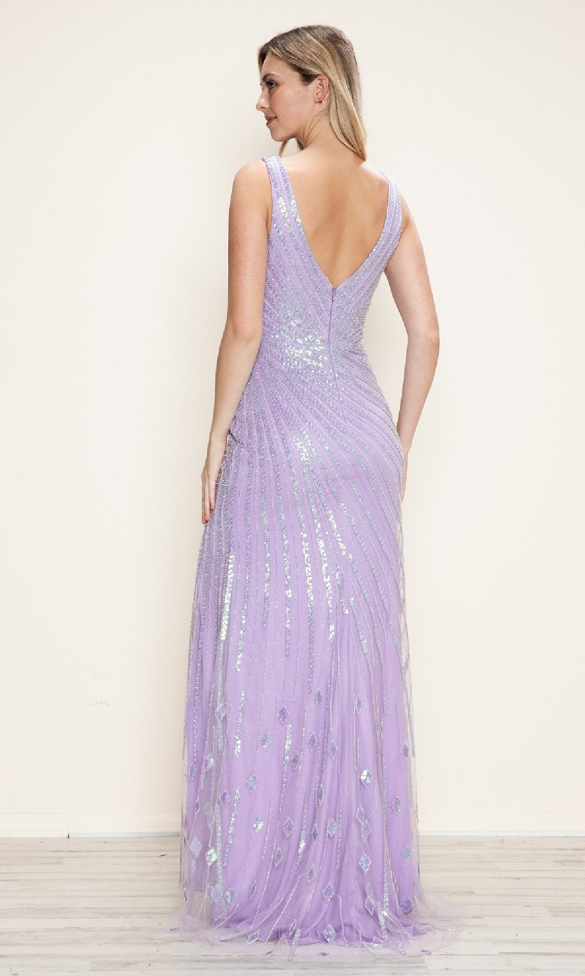 A woman faces away, wearing the Poly USA 9522 Deep V-Neck Long Sequin Prom Dress—sleeveless, floor-length, light purple with a deep V-back—set against a plain light background.