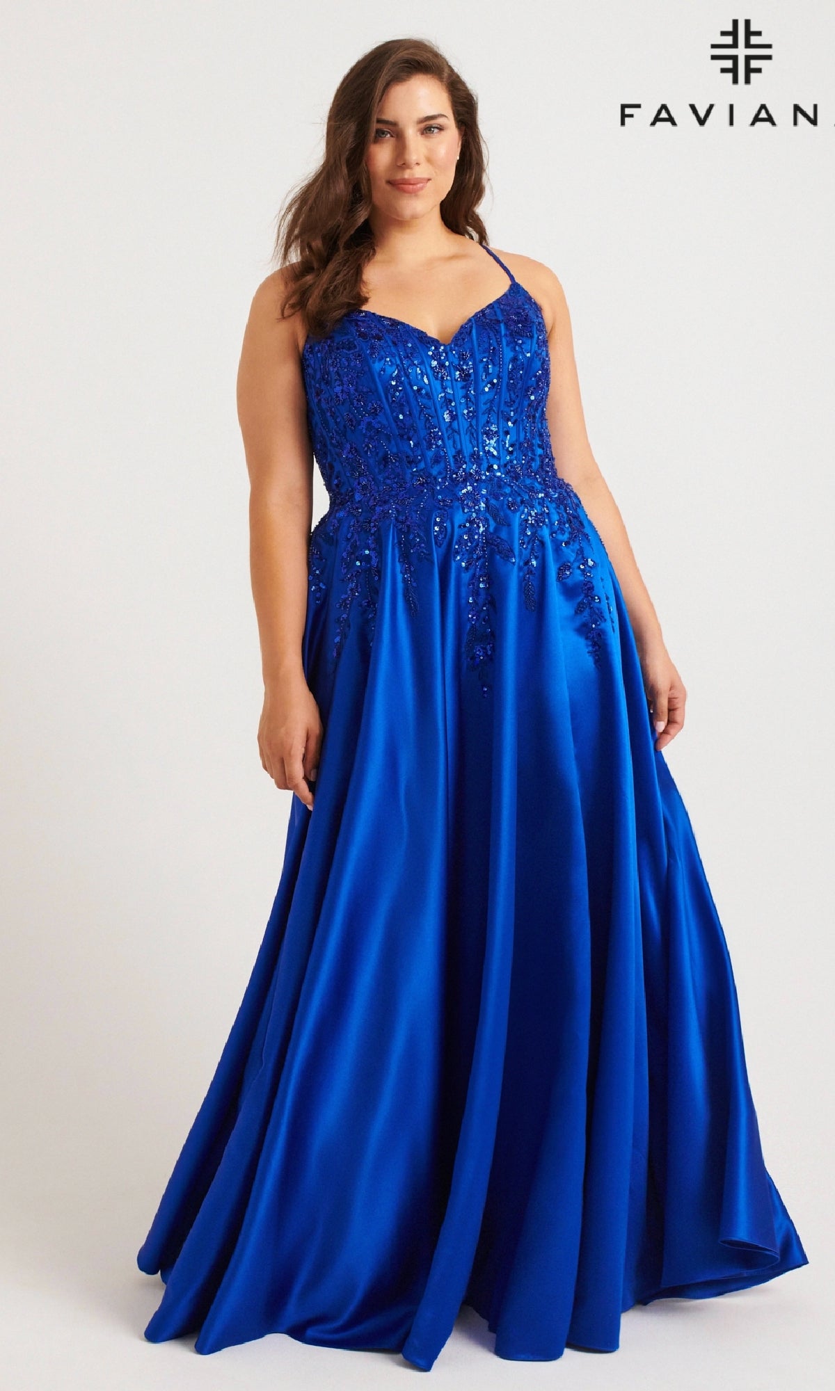 A woman wears the Faviana 9575, a long plus-size royal blue sequin prom dress with a fitted bodice and flared skirt. The floor-length gown sparkles with embellishments, set against a plain background. The FAVIANA logo appears in the top right corner.