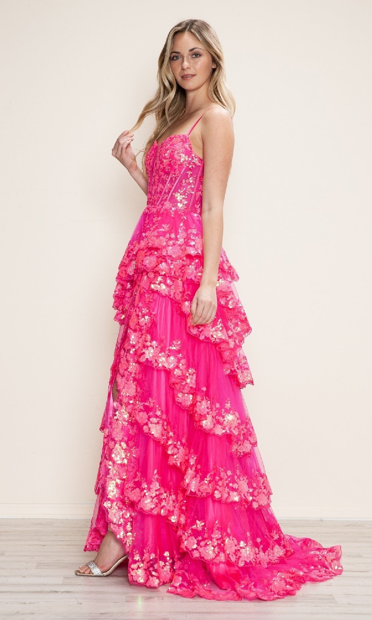 A woman poses indoors in the Poly USA 9606 long prom dress—bright pink, flowy with spaghetti straps, metallic floral embellishments, and a tiered A-line silhouette—set against a neutral background.