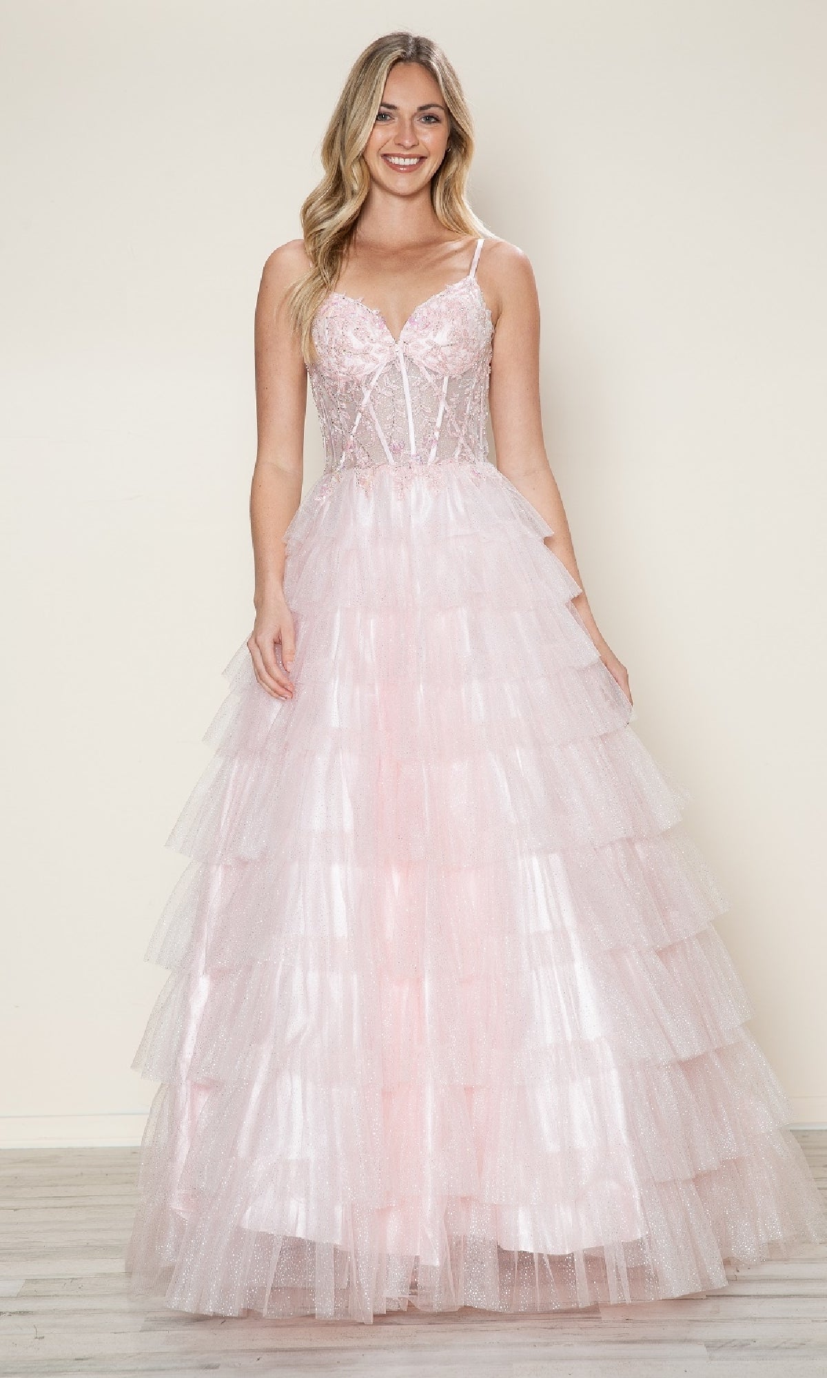 A woman smiles at the camera in the Poly USA 9608 Long Prom Dress, featuring light pink ruffles, a fitted lace corset bodice, and a tiered skirt, standing against a plain background.