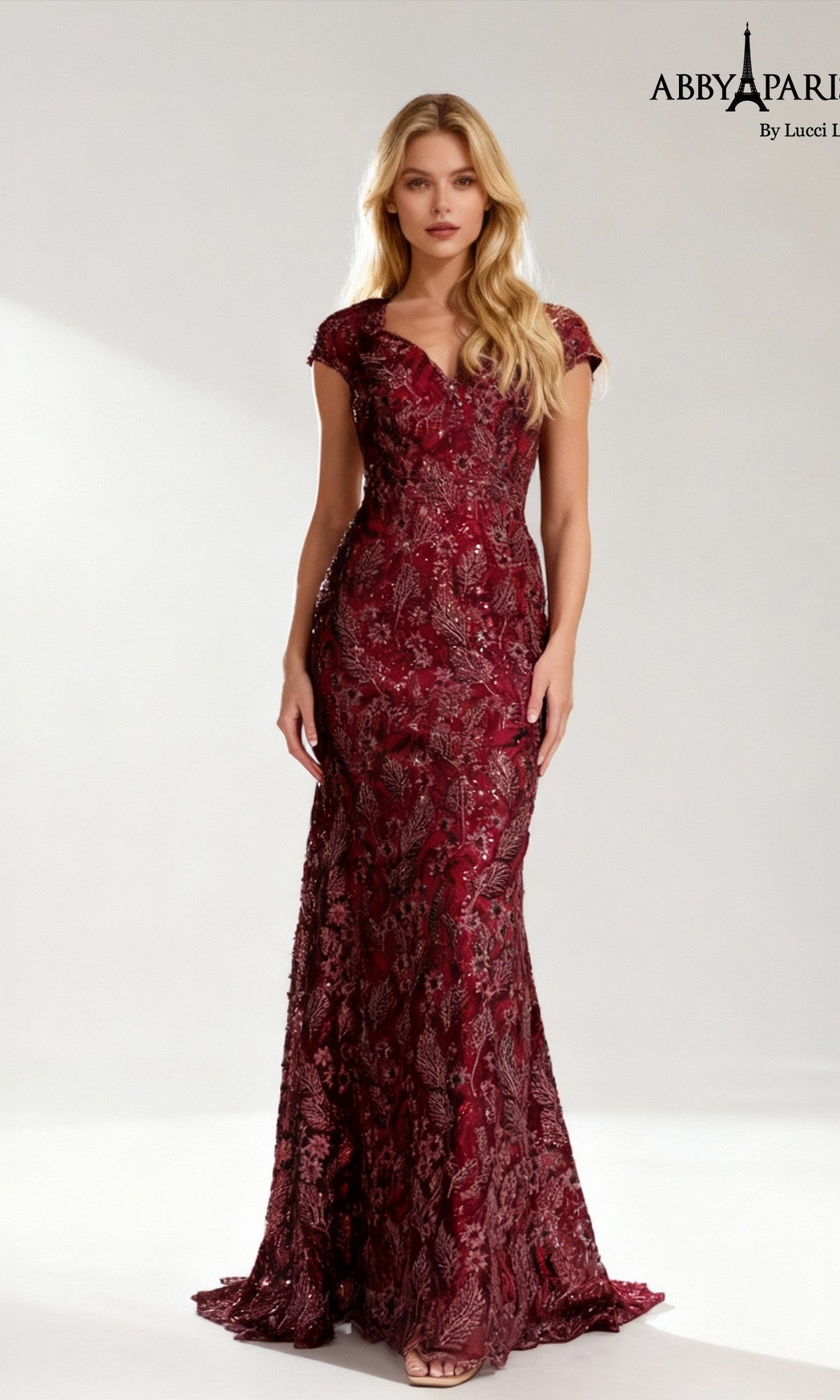 A woman wearing the Abby Paris 96096, a floor-length formal dress in wine with short sleeves, featuring intricate floral lace detailing and a graceful sheath silhouette, stands against a plain light background—an elegant and stunning choice for the mother of the bride.