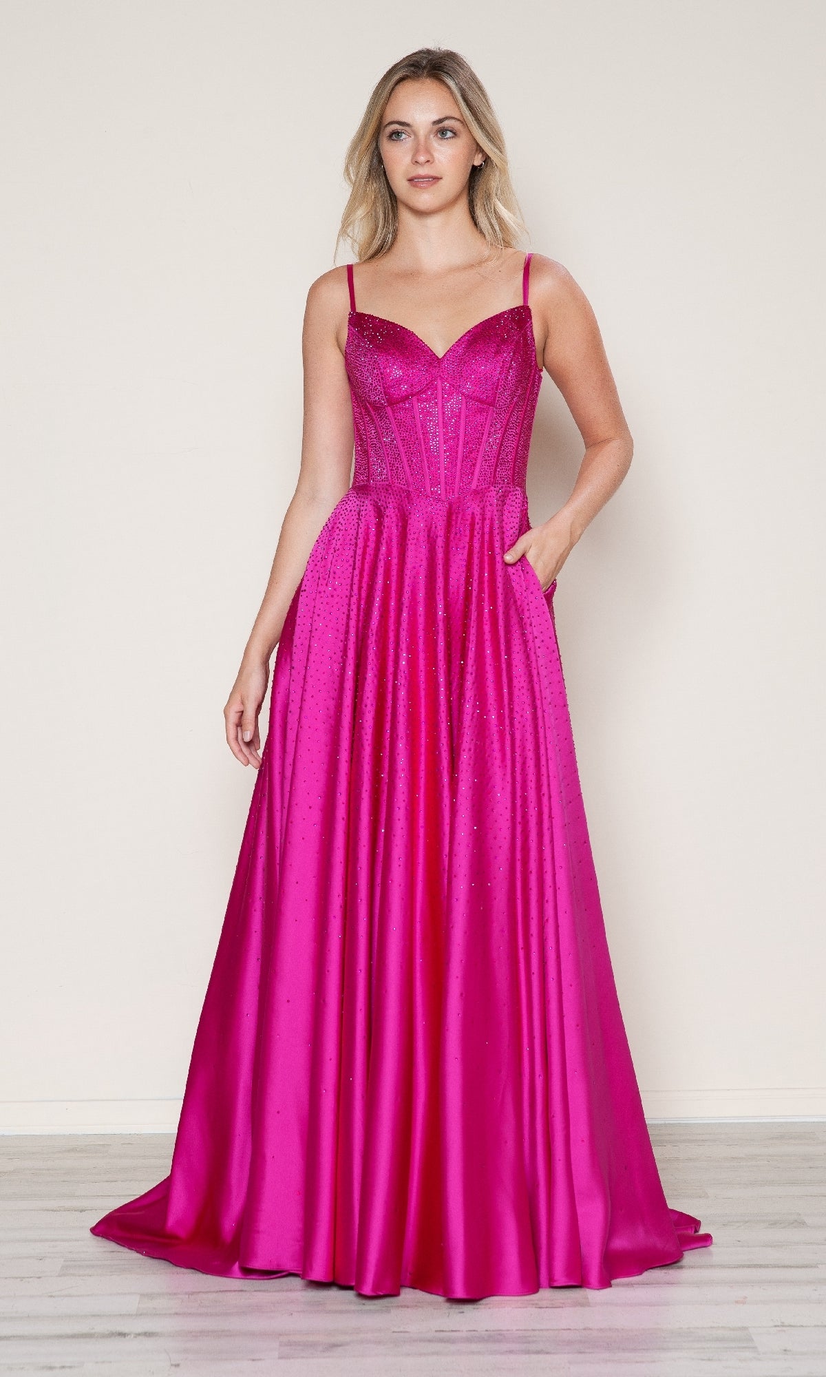 A woman models the Long Prom Dress: Poly USA 9610—an a-line, floor-length, bright pink gown with spaghetti straps and a fitted corset bodice—standing against a plain light background.