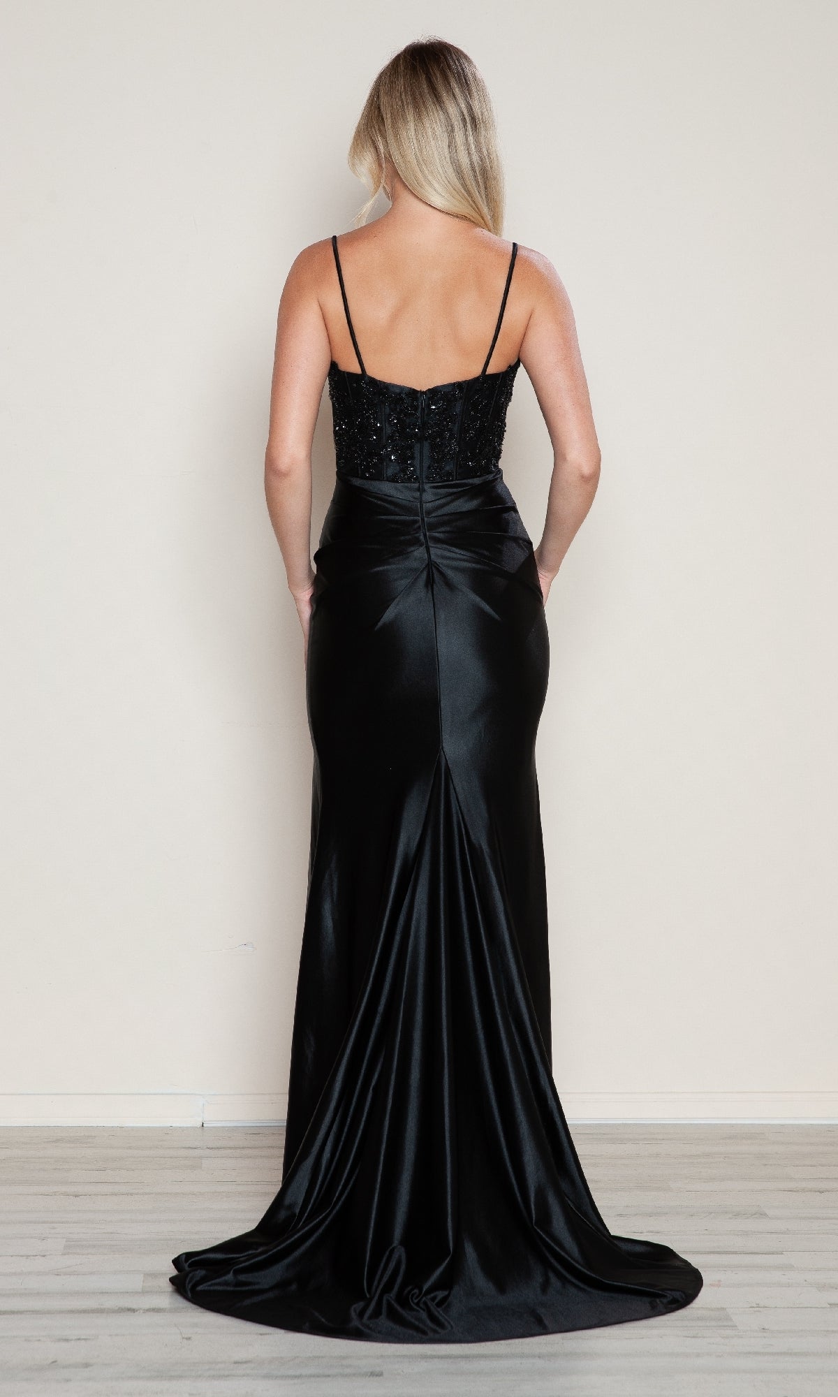 A woman stands facing away in the Beaded-Bodice Long Prom Dress by Poly USA 9616, featuring a beaded corset bodice with thin straps and a flowing satin skirt that forms a small train.