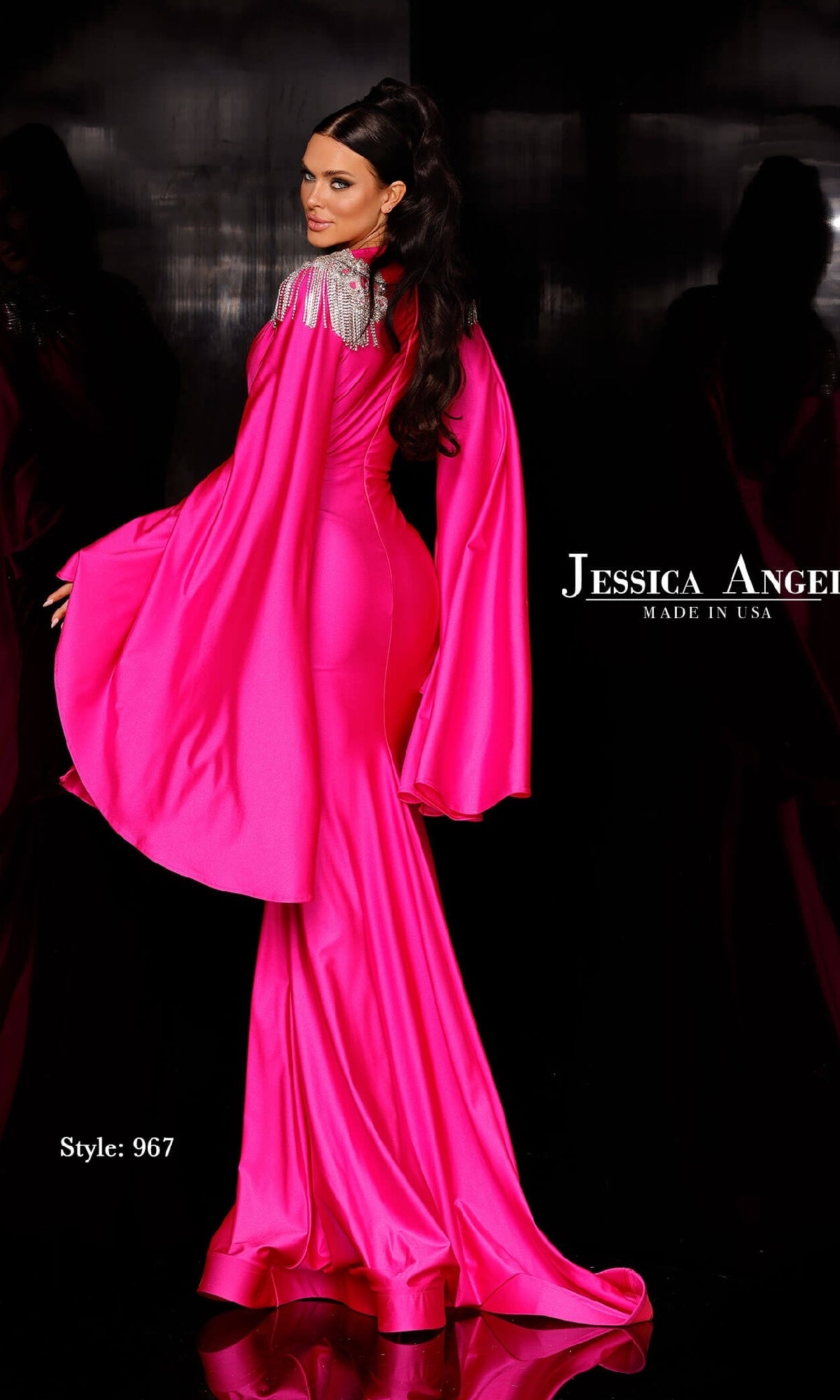A woman poses against a black background in the Long Cape-Sleeve Formal Dress: Jessica Angel 967—a bright pink gown with dramatic cape sleeves and silver shoulder accents.