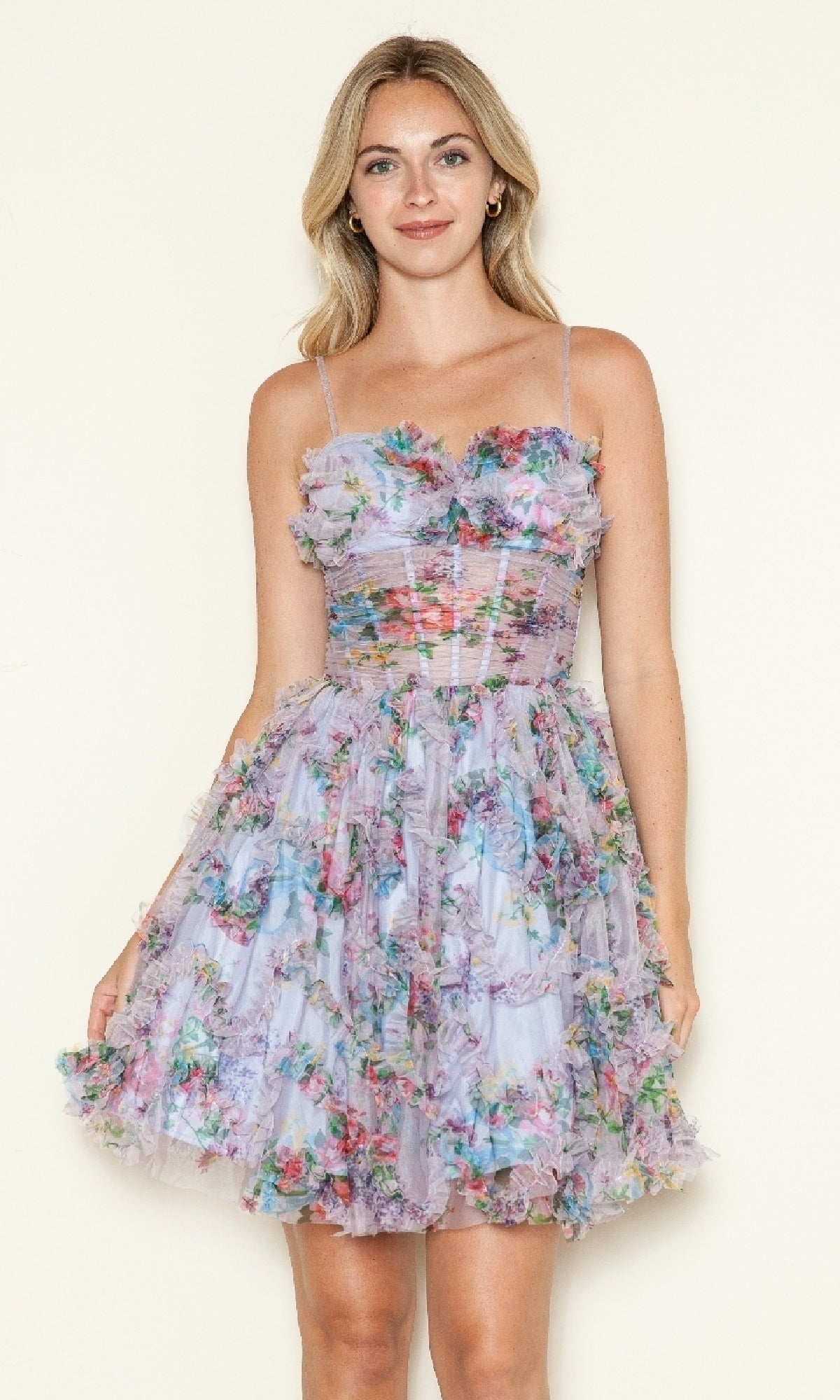 A woman poses against a plain background, wearing the Short Lavender Print Hoco Dress: Poly USA 9672—a sleeveless, knee-length, floral tulle dress with spaghetti straps and a fitted bodice.