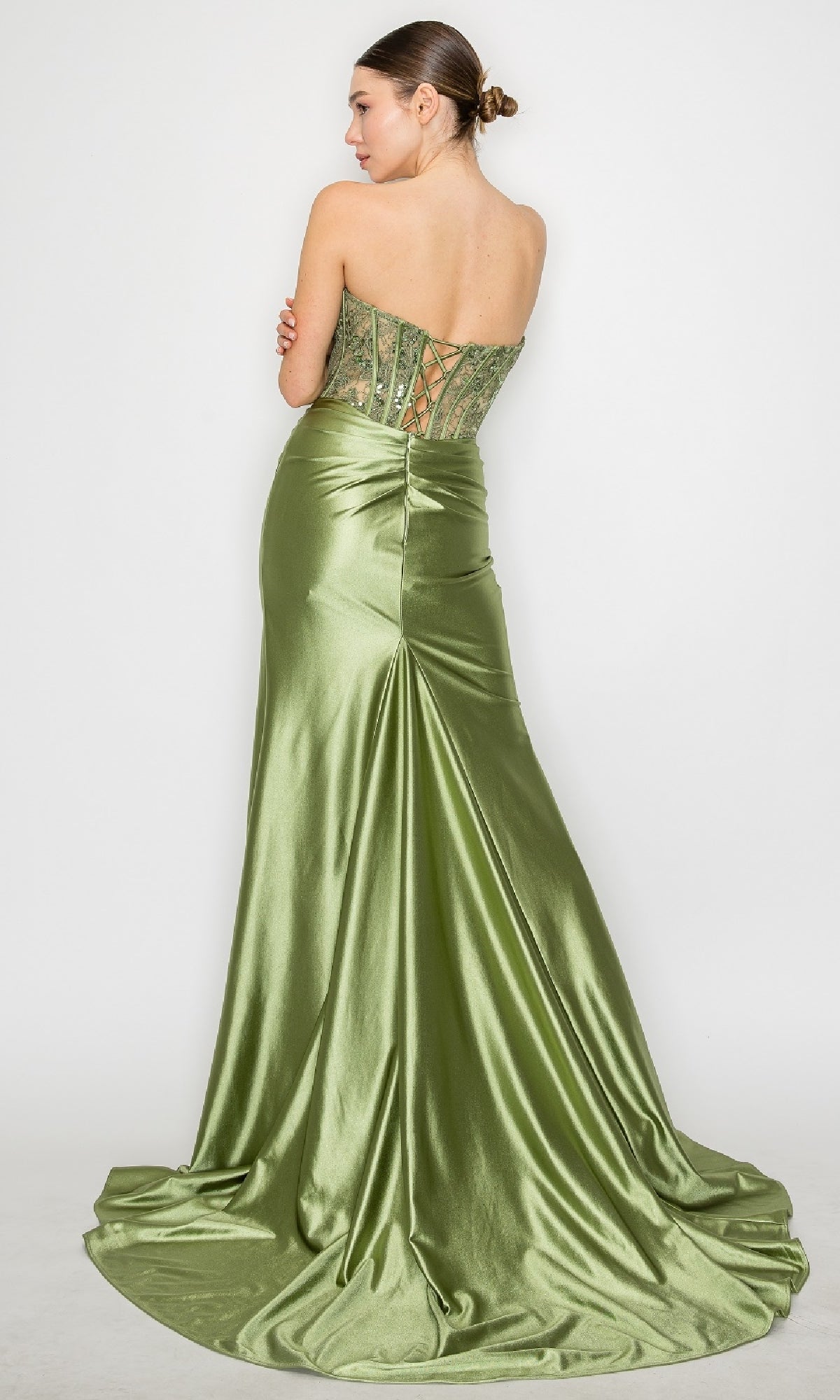 A woman wears the Strapless Long Corset Prom Gown: Poly USA 9688, showcasing its green satin finish, lace-up back, sheer lace corset bodice, and flowing train as she stands against a plain white background.